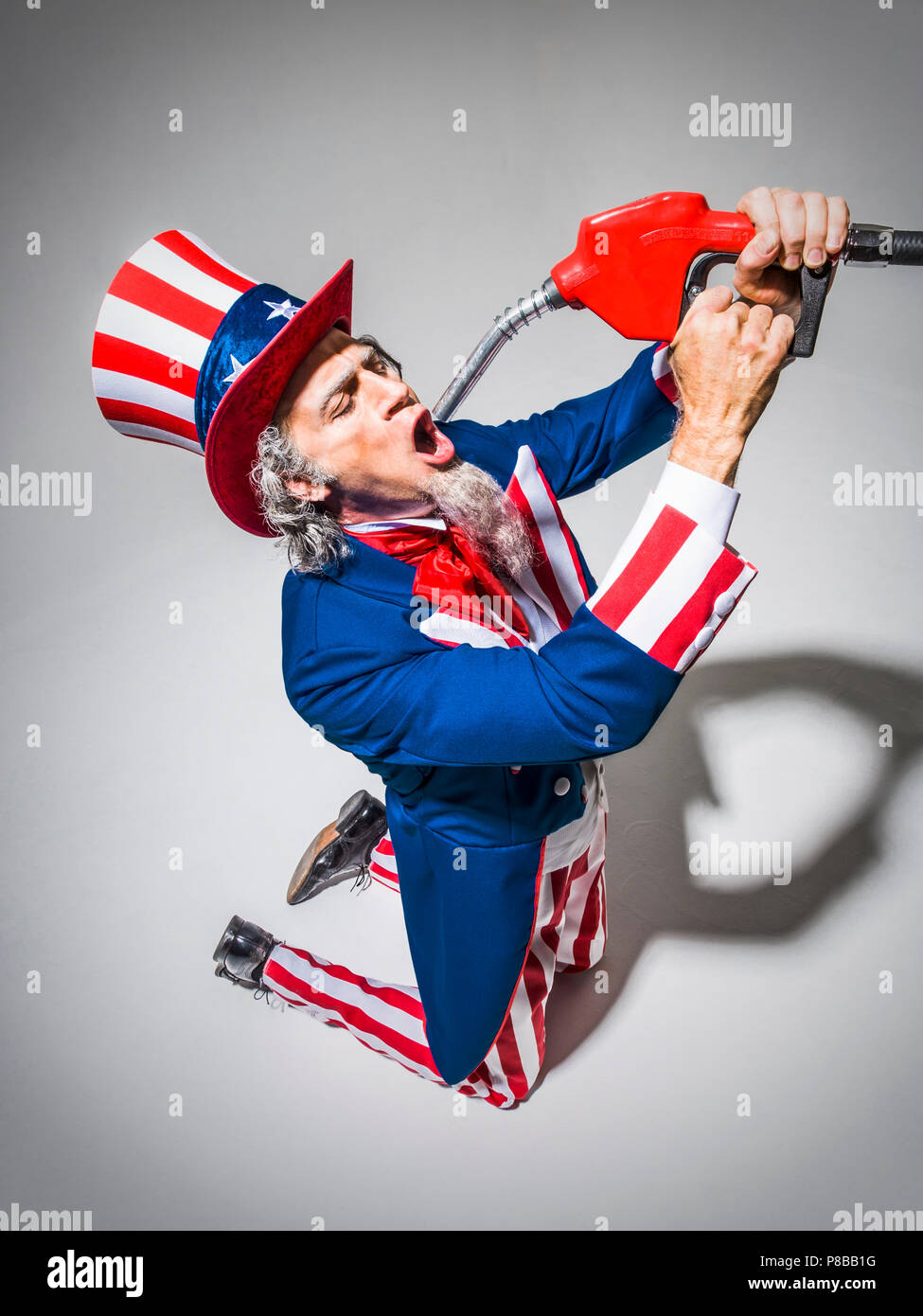 L'Oncle Sam à genoux avec une buse de la pompe à gaz qui a eu lieu en face de sa bouche comme s'il allait boire de l'essence. Shot conceptuel illustrant l'American addict Banque D'Images