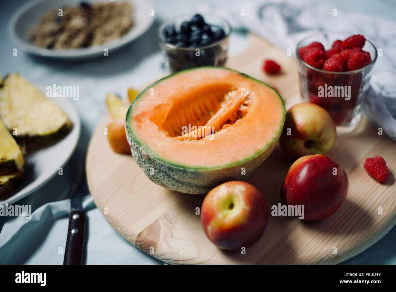 Saine alimentation végétalien végétarien savoureux petit-déjeuner détox avec fruits frais de saison et de baies servi sur planche à découper sur fond bleu pastel Banque D'Images