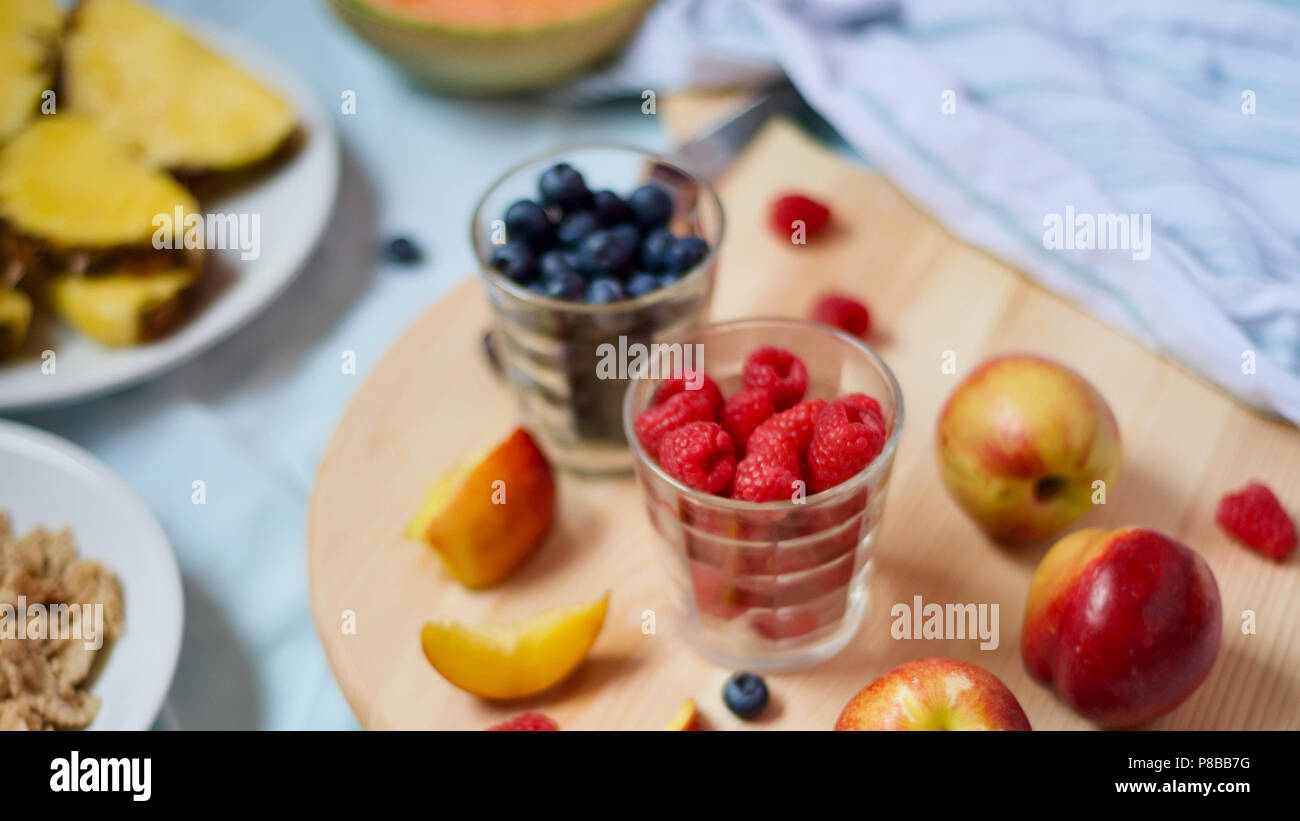 Saine alimentation végétalien végétarien savoureux petit-déjeuner détox avec fruits frais de saison et de baies servi sur planche à découper sur fond bleu pastel Banque D'Images