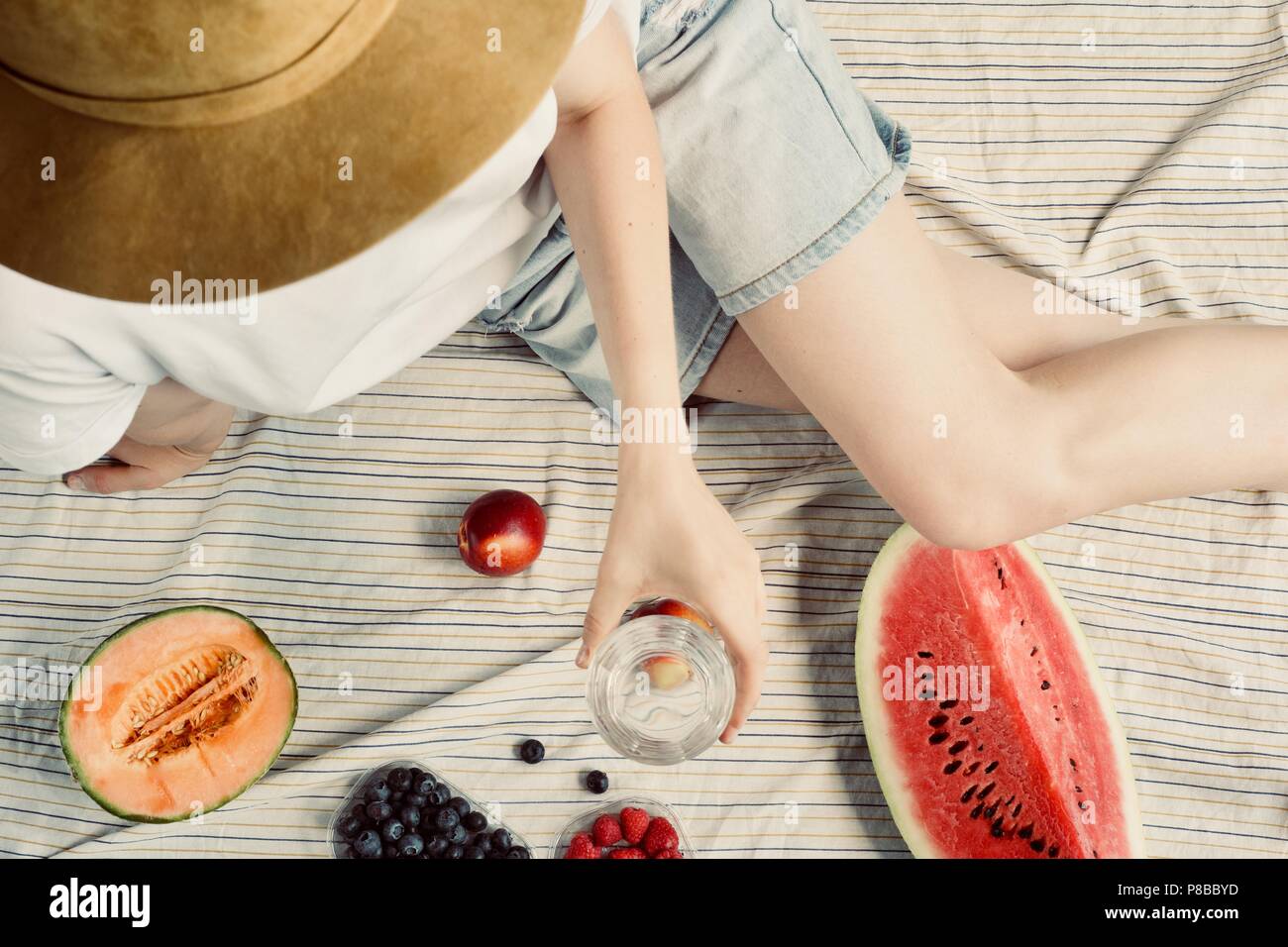 Pique-nique d'été. Short femme en jean et eatining chapeau melon d'eau, melon, les bleuets, les framboises et les pêches, l'eau potable. Gatheri en plein air Banque D'Images