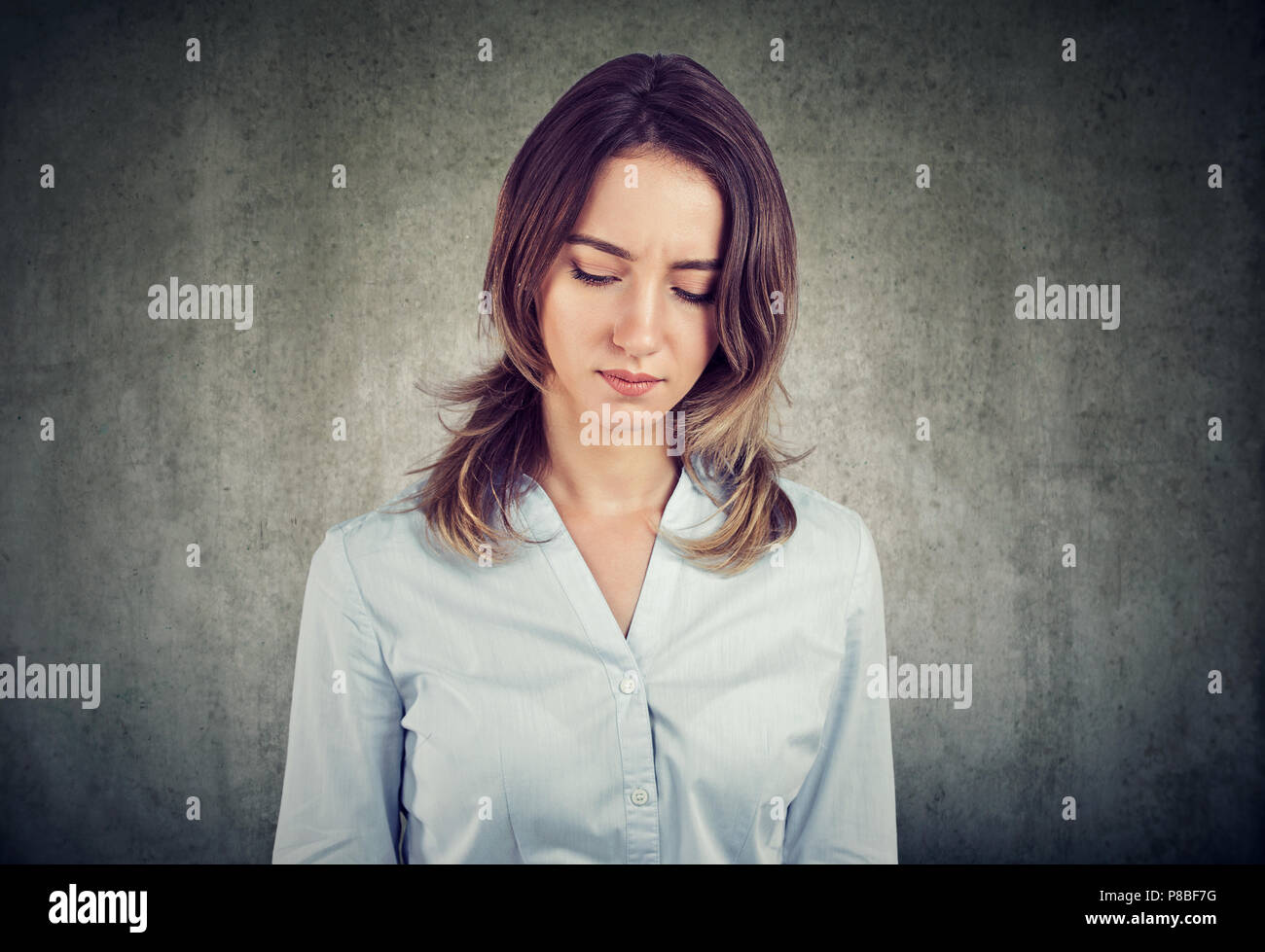 Très jolie chemise femme en regardant vers le bas en sombre et d'émotions à la colère sur fond gris Banque D'Images