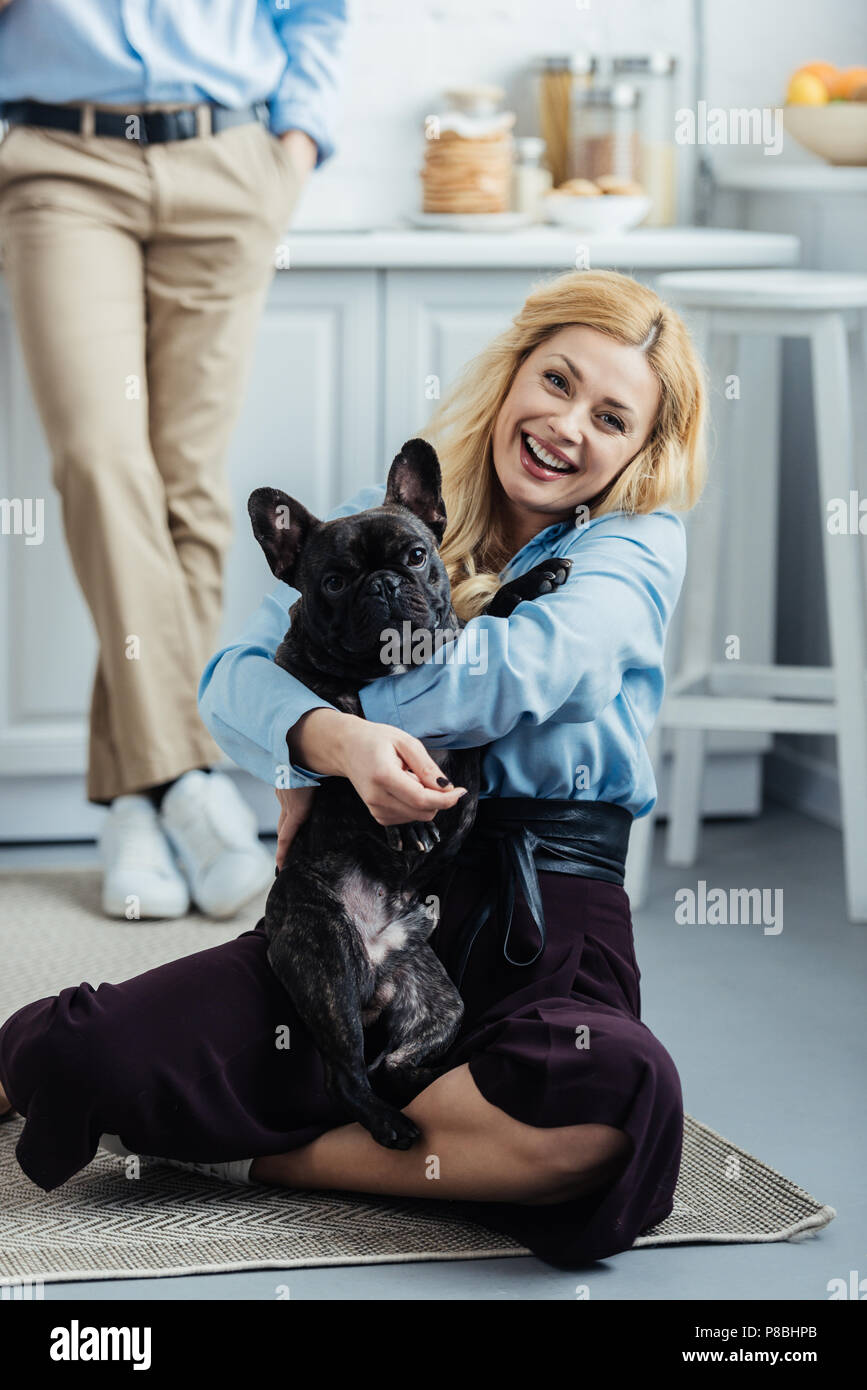 Homme debout par happy woman hugging bouledogue français sur le sol de la cuisine Banque D'Images