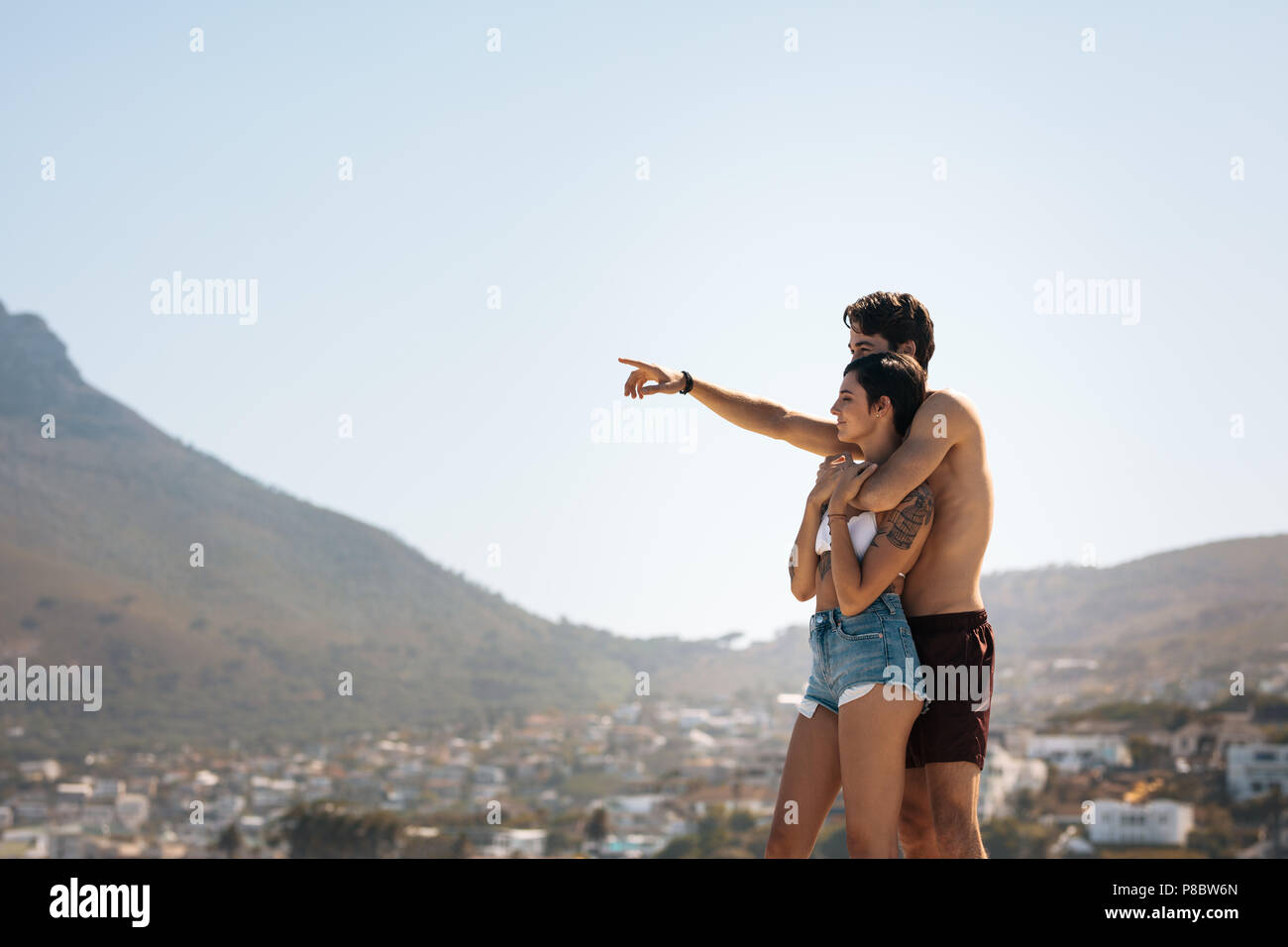 Couple debout sur une colline et en regardant la ville en bas de la colline. Homme tenant la femme par derrière et pointant vers quelque chose. Banque D'Images