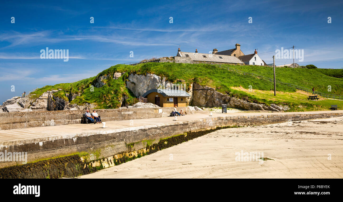 Royaume-uni, Irlande du Nord, Co Antrim, Islandmagee, Portmuck, les visiteurs assis dans soleil sur mur du port, vue panoramique Banque D'Images