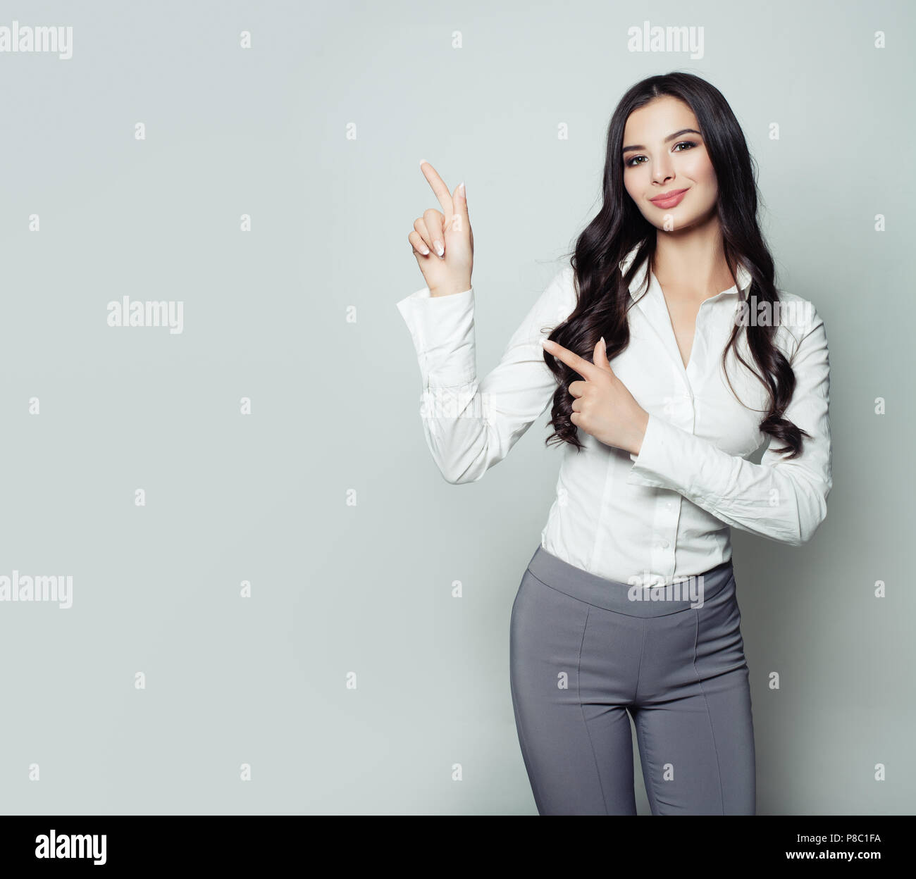 Jeune femme d'affaires pointant son doigt vers le haut sur fond gris avec copie espace. Friendly woman portrait, publicité marketing et le placement de produit c Banque D'Images