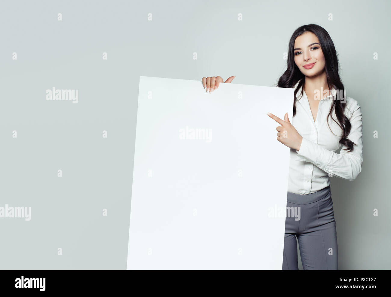 Jeune femme d'affaires avec le blanc du papier vierge bannière pointant son doigt. Smiling woman portrait, concept d'affaires et d'éducation Banque D'Images