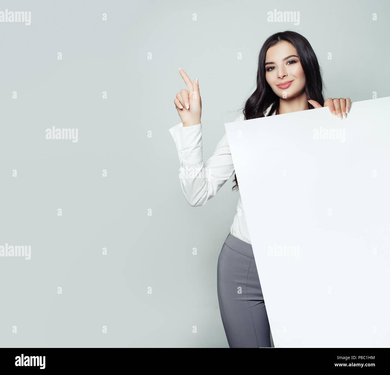 Business Woman portrait. Businesswoman pointing à fond gris et vide holding white bannière. Référencement et publicité marketing concept Banque D'Images