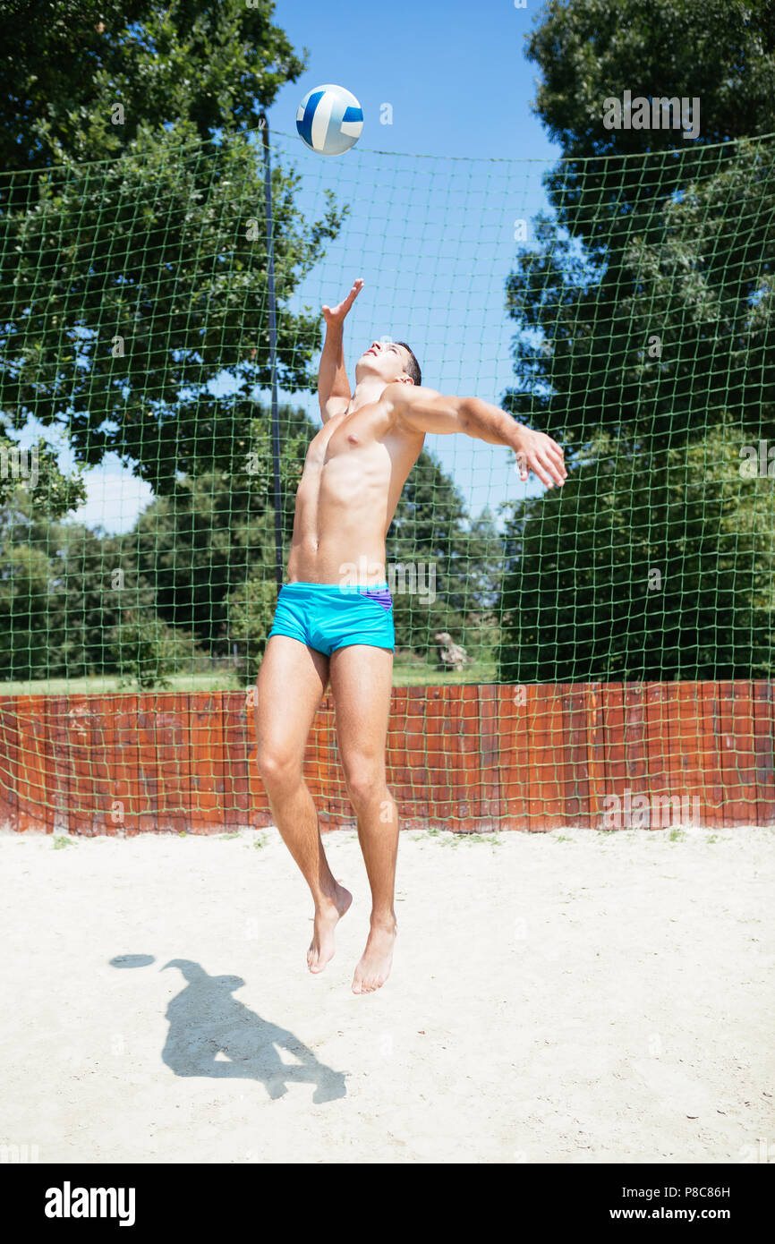 Beach-volley - bel homme jeune à jouer au volleyball de plage. Chaude journée d'été. Banque D'Images