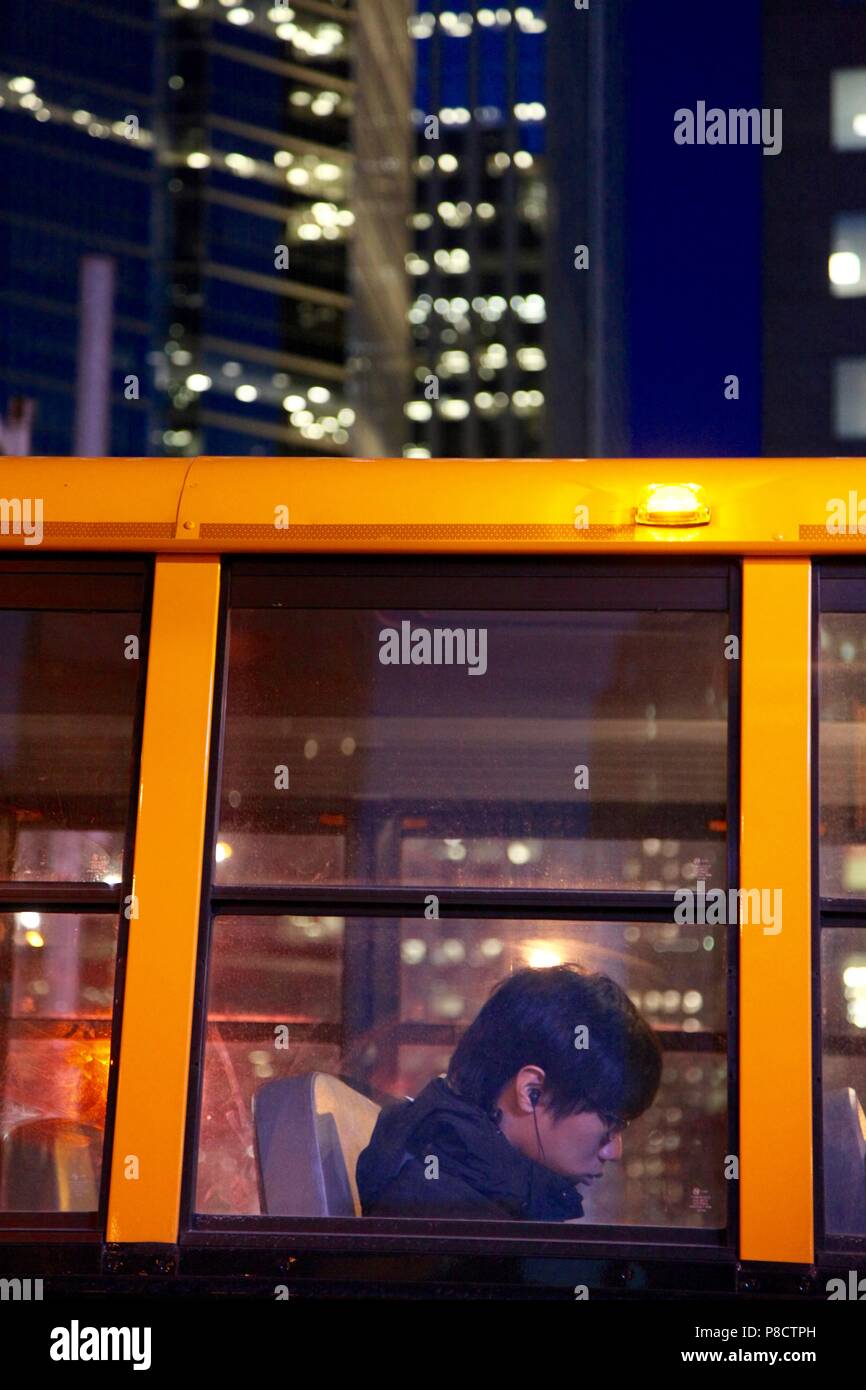 Jeune homme asiatique en prenant un bus scolaire dans la nuit avec les lumières de la ville urbaine dans l'arrière-plan Banque D'Images