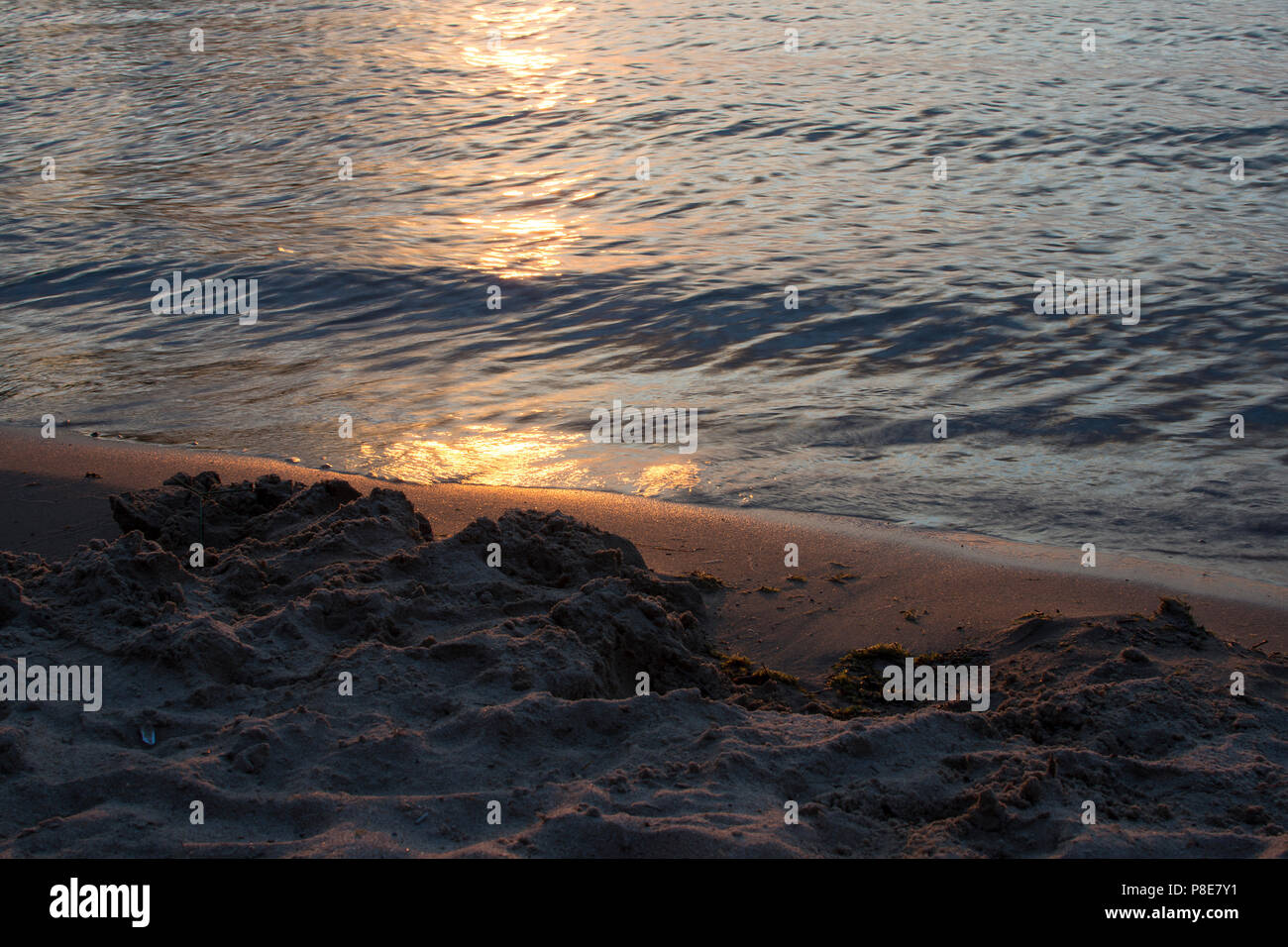 Gros plan du sable sur la plage éblouissante avec la réflexion du soleil dans l'eau. Banque D'Images