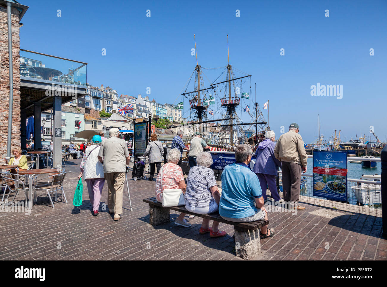 23 Mai 2018 : Brixham, Devon, UK - Personnes âgées La détente sur le front de mer à Brixham Harbour, avec la réplique Golden Hind voilier. Banque D'Images