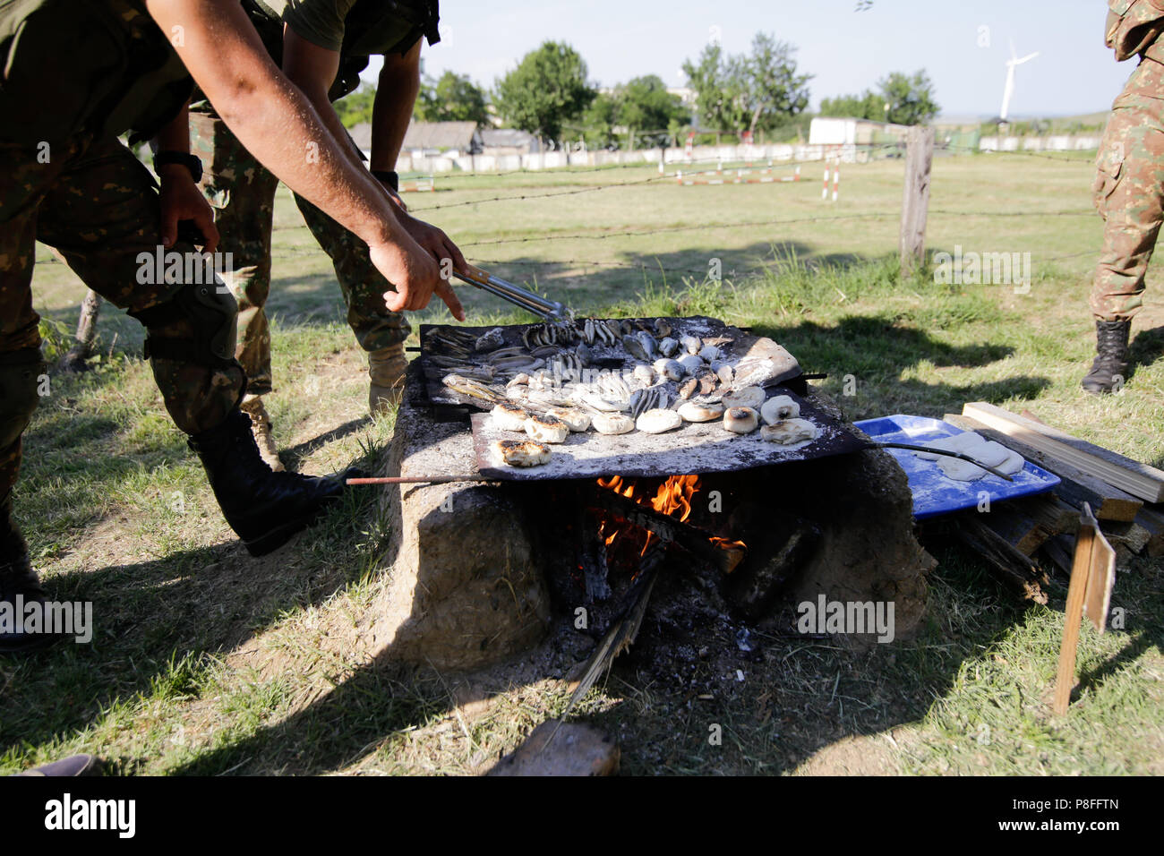 La préparation des soldats repas sur une grille à la main en bois ouverte sur le feu, à un camp de survie. Ils cuisent des serpents d'eau, les poissons, les grenouilles et le pain. Banque D'Images