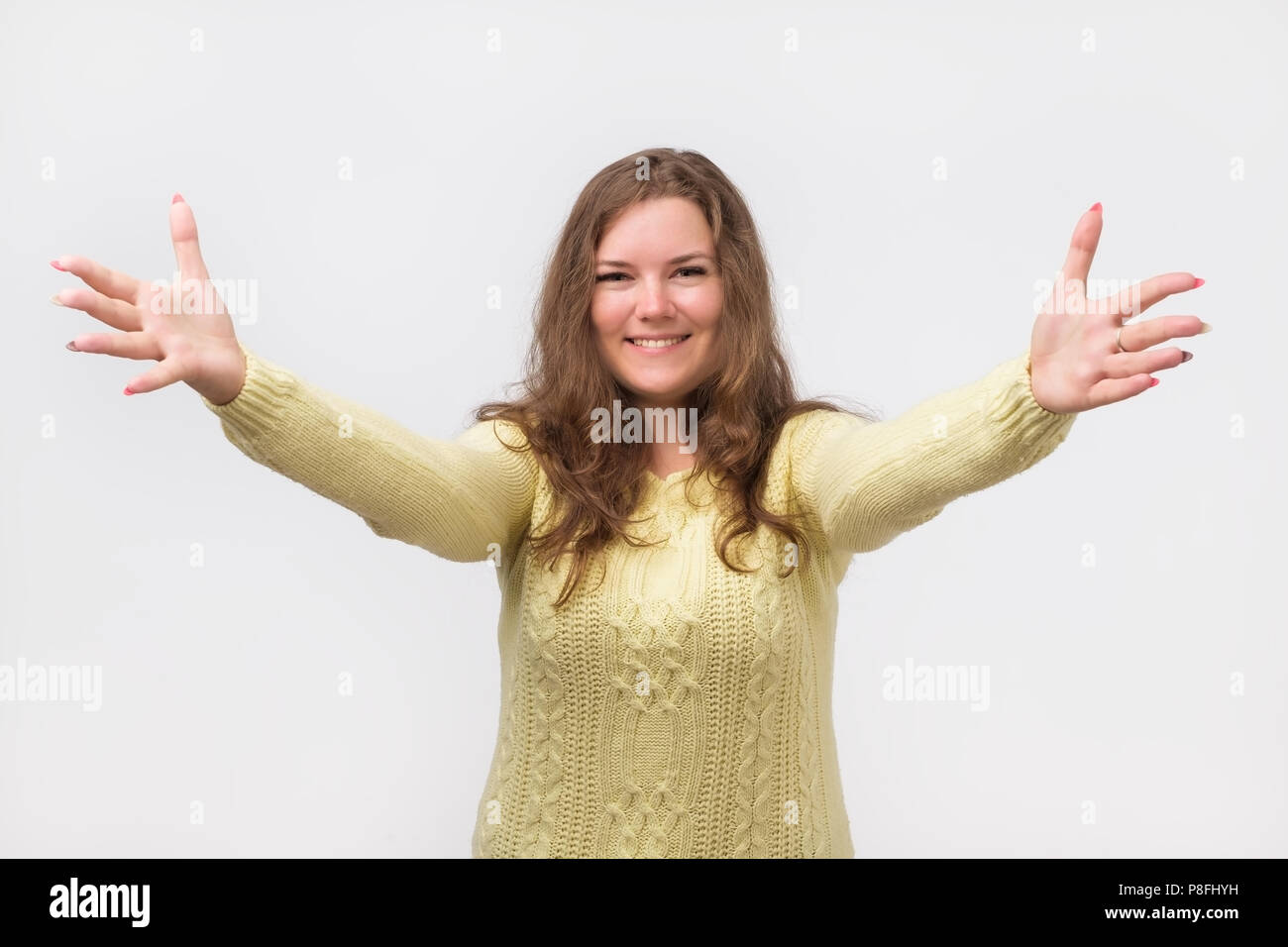 Portrait of attractive smiling caucasian woman soulevées jusqu'aux mains à vous. Elle est habillée en jaune pour homme. Heureux d'accueillir un(e) ami(e) ou invité. J'wa Banque D'Images