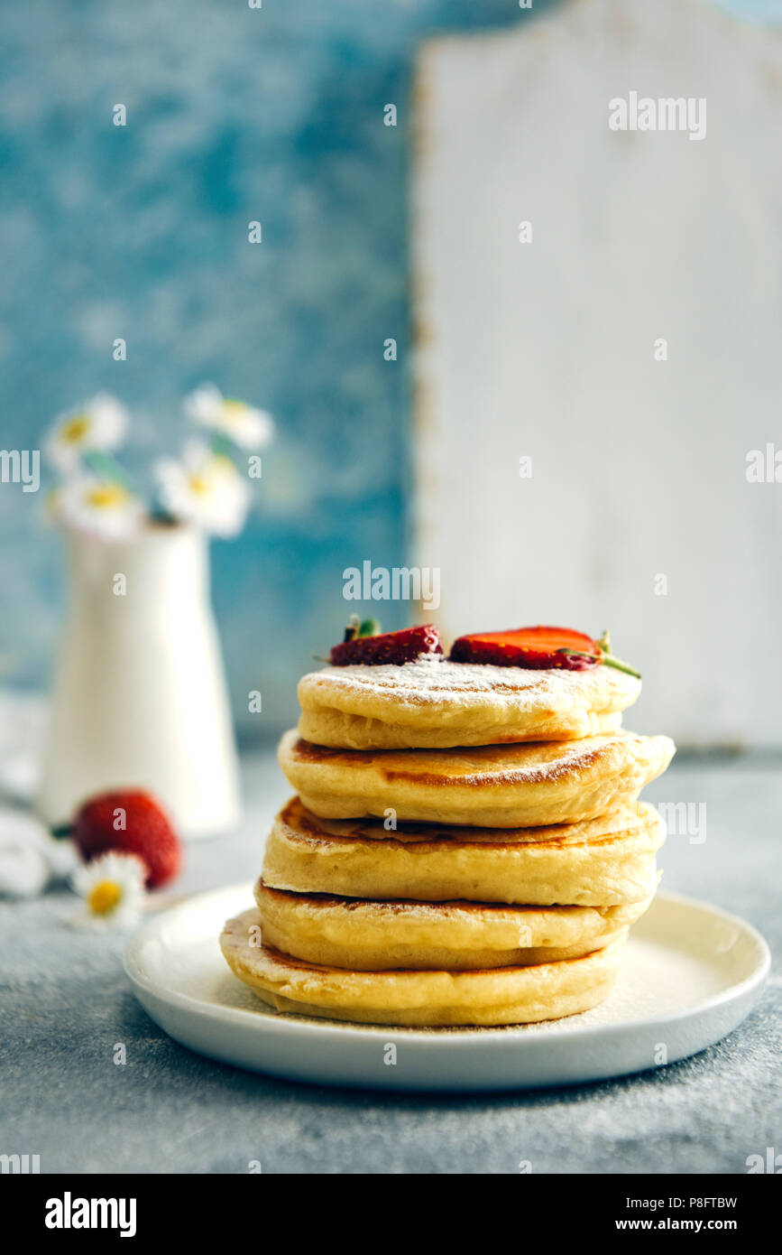 Le lait d'Amande crêpes garnies de fraises et de sucre en poudre empilés sur une assiette blanche photographié à partir de la vue de face. Les fraises et les fleurs accom Banque D'Images