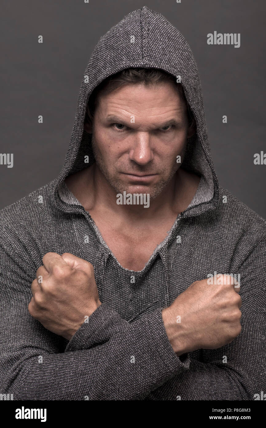 L'expression intense de tough man wearing sweater sweat gris et fléchis poings croisés sur fond gris Banque D'Images