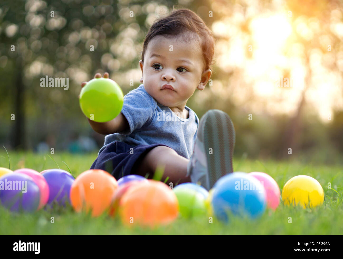 Cute asian baby boule colorée en vert de l'herbe - Coucher de soleil effet du filtre Banque D'Images