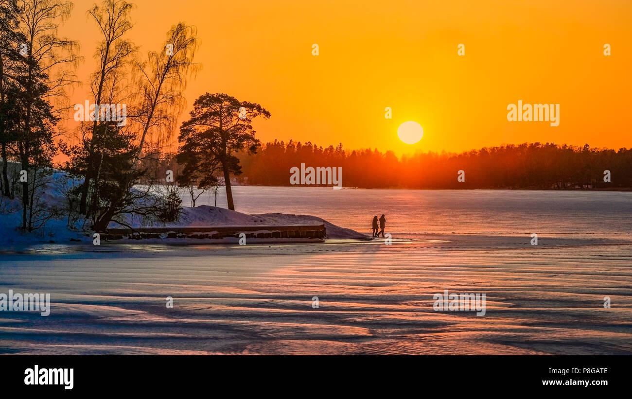 Un couple de touristes promenades romantiques en Laponie sur un lac de glace sur un coucher de soleil. Vue extérieure d'hiver de l'atmosphère. Banque D'Images
