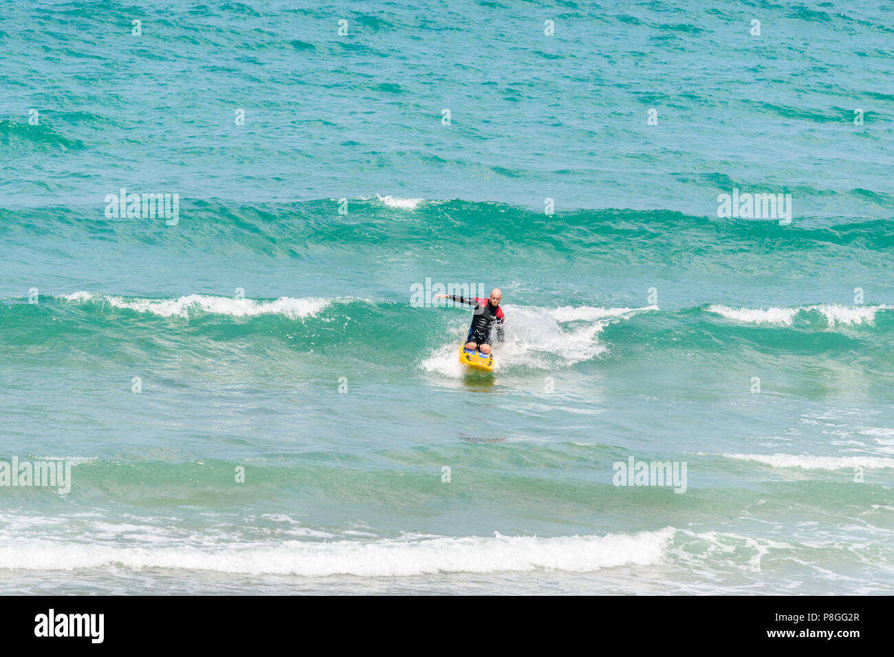 Un maître-nageur masculin avec une vague surfe surf de l'océan Atlantique, ses vagues frapper la plage sablonneuse, au village de St Agnes, Cornwall, Angleterre. Banque D'Images