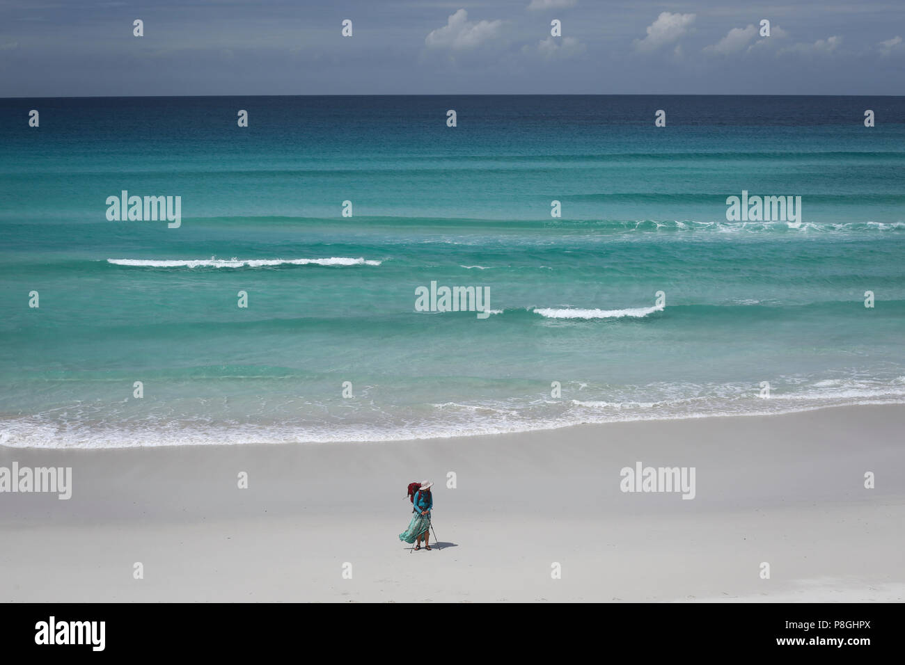 Female hiker marchant le long d'une plage de sable blanc avec une mer. Banque D'Images