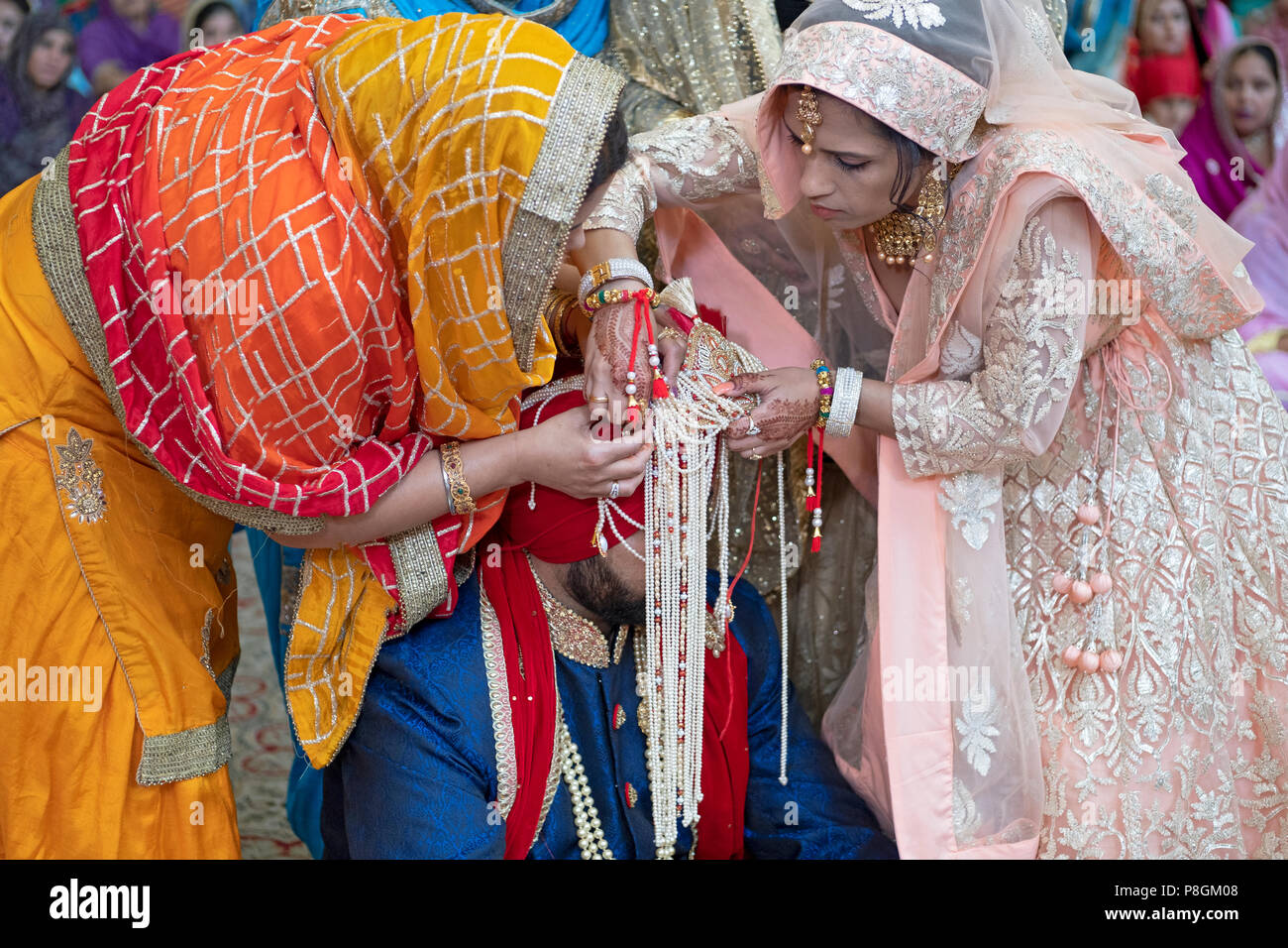Les femmes dans le cortège fixer le turban du marié à une cérémonie de mariage dans le temple à la Sikh Society à Richmond Hill, Queens, New York. Banque D'Images