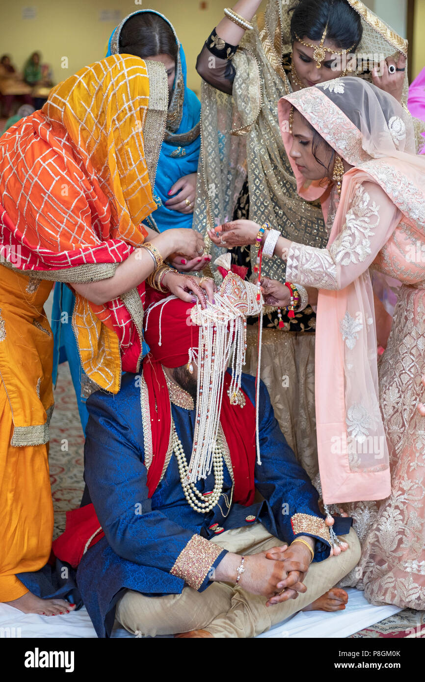 Les femmes dans le cortège fixer le turban du marié à une cérémonie de mariage dans le temple à la Sikh Society à Richmond Hill, Queens, New York. Banque D'Images