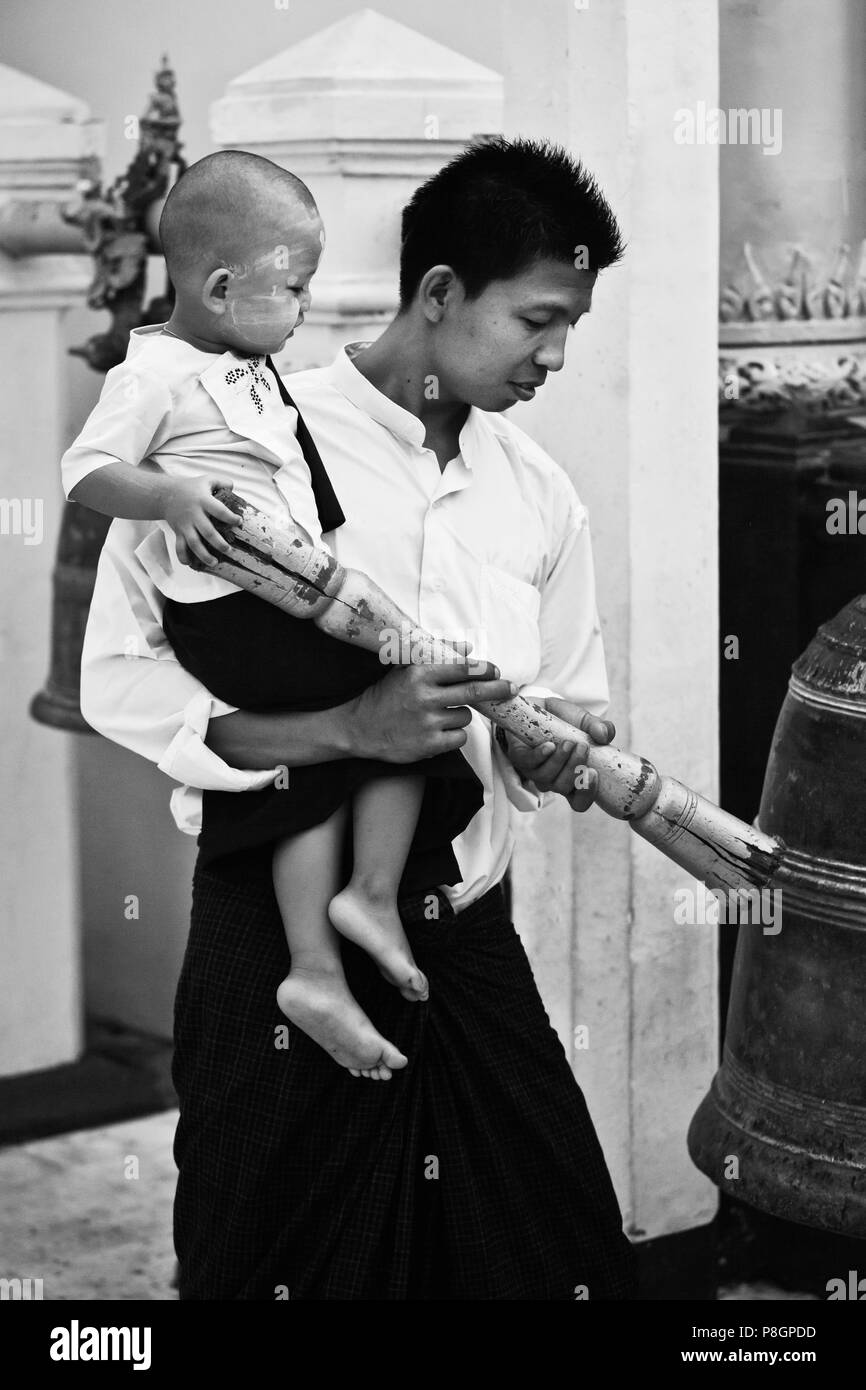 Homme birman avec fils sonne une cloche à la PAYA SHWEDAGON PAGODA ou qui remonte au temps du Bouddha - Yangon, Myanmar Banque D'Images