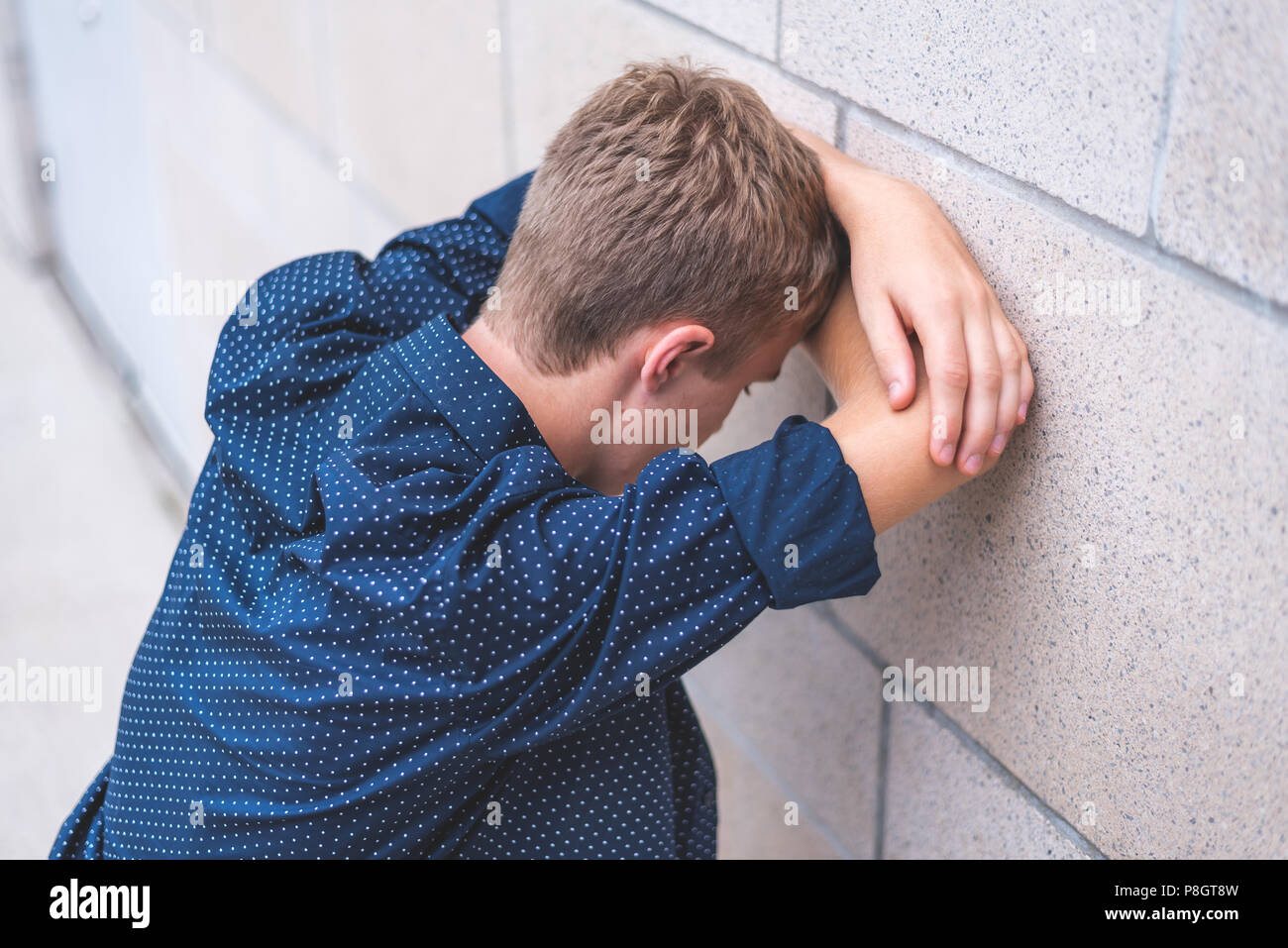Pleurer dans l'adolescence, les bras croisés contre un mur de briques. Banque D'Images
