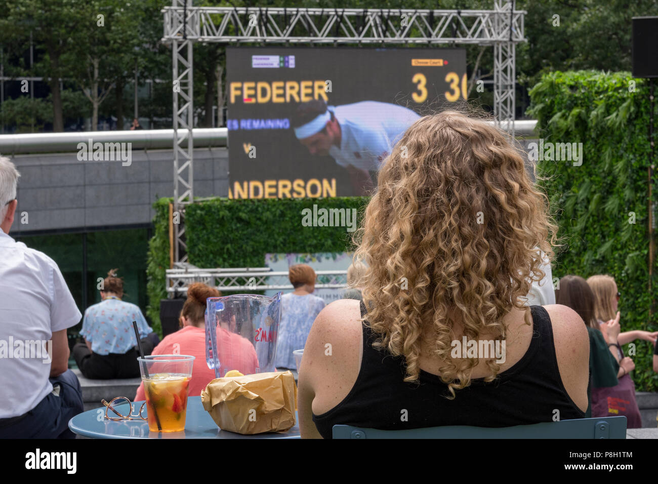 London, UK.11 juillet 2018. L'écope, More London place, au centre de Londres. Une jeune femme assise avec une boisson fraîche regarde le tennis de Wimbledon 2018 sur un grand écran dans le cadre de l 'été par le fleuve" initiative comme Roger Federer perd son match de quart de finale contre Kevin Anderson et perd sa chance de réaliser son rêve de gagner un autre grand chelem championnat. Crédit : Steve Hawkins Photography/Alamy Live News Banque D'Images