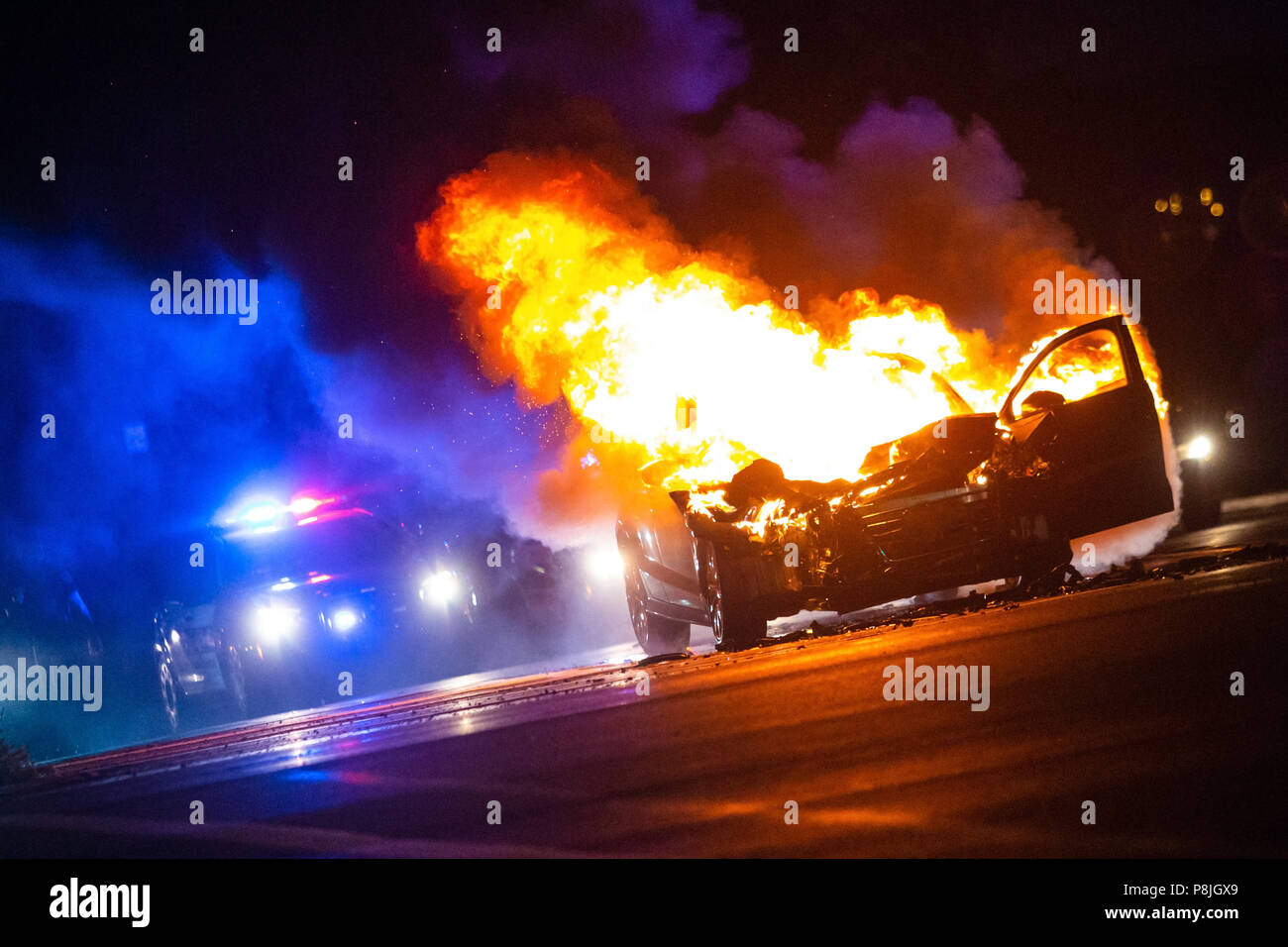 Voiture en feu dans la nuit avec les lumières de police en arrière-plan noone Banque D'Images