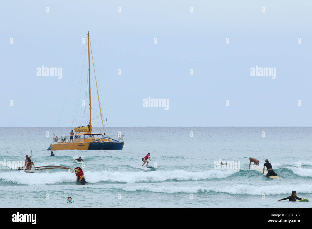 Bateau à voile nommé Manu Kai pour les touristes. Les surfeurs et les gens dans l'eau sont visibles. La plage de Waikiki, Waikiki, Honolulu, Oahu, Hawaii, USA. Banque D'Images