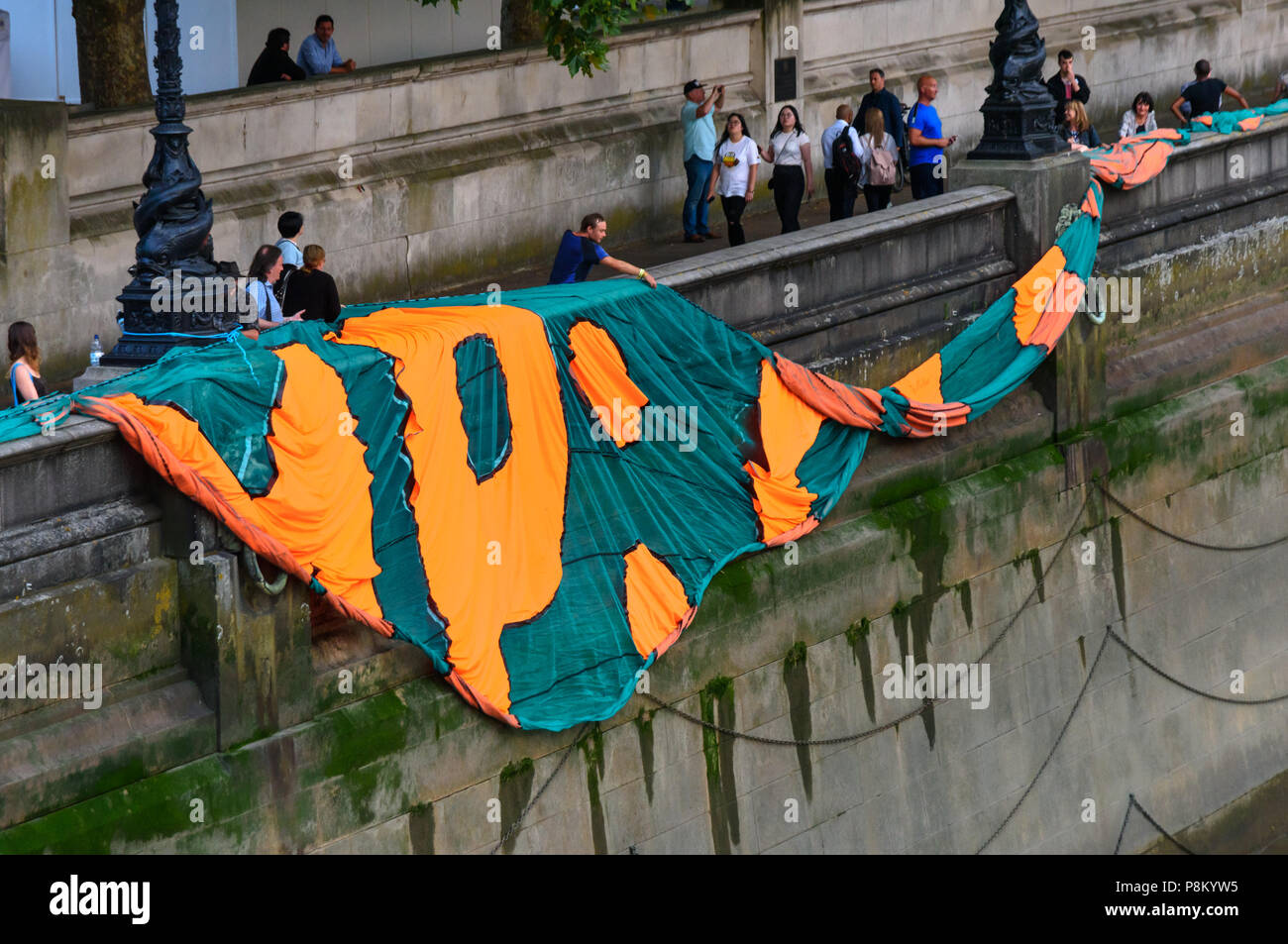 Londres, Royaume-Uni. 12 juillet 2018. Les militants climatiques commencent à laisser tomber leur bannière géante de 100 mètres de longueur le long de la berge de la Tamise en face de la Chambre du Parlement où ils vont à l'afficher à l'occasion de la visite d'Atout au Royaume-Uni. La bannière a porté le message 'TRUMP : génocide climatique" en lettres orange fluorescent autour de 15m de haut. Ils disent qu'il est ignorant délibérément la science sur le changement climatique et menace l'existence même de la vie humaine sur terre en sapant si ce n'est pas renverser les nous et les efforts mondiaux pour lutter contre la plus grande menace que l'humanité fait face aujourd'hui, la catastrophique destabilis Banque D'Images