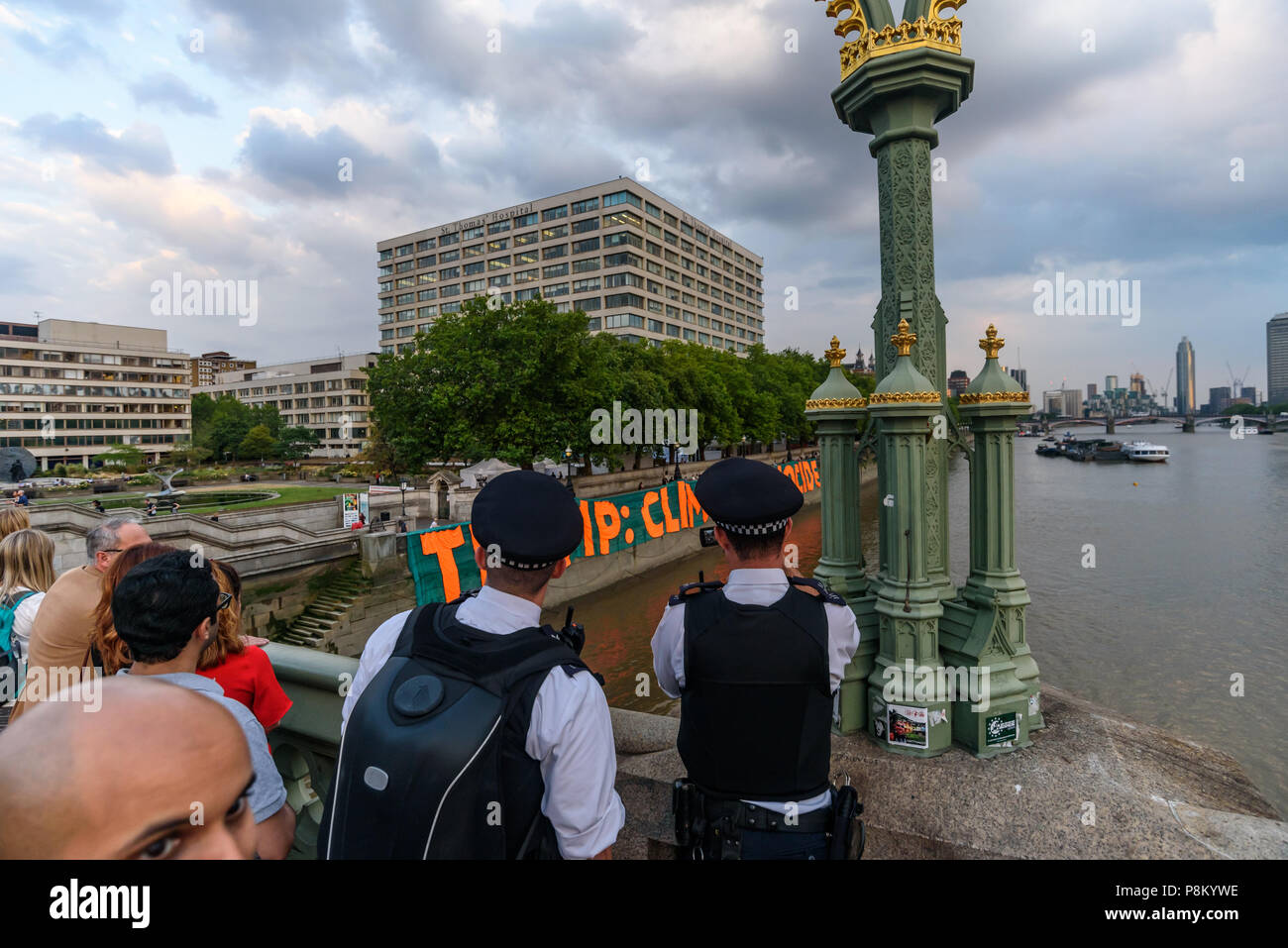 Londres, Royaume-Uni. 12 juillet 2018. La police et de nombreux touristes et de regarder le film comme activistes du climat mark Trump à l'occasion de sa visite au Royaume-Uni en laissant tomber une bannière géante de 100 mètres de long sur la rivière mur de la Tamise en face du Palais de Westminster. La bannière a porté le message 'TRUMP : génocide climatique" en lettres orange fluorescent autour de 15m de haut. Ils disent qu'il est ignorant délibérément la science sur le changement climatique et menace l'existence même de la vie humaine sur terre en sapant si ce n'est pas renverser les nous et les efforts mondiaux pour lutter contre la plus grande menace que l'humanité fait face aujourd'hui, la déstabilisation catastrophique Banque D'Images