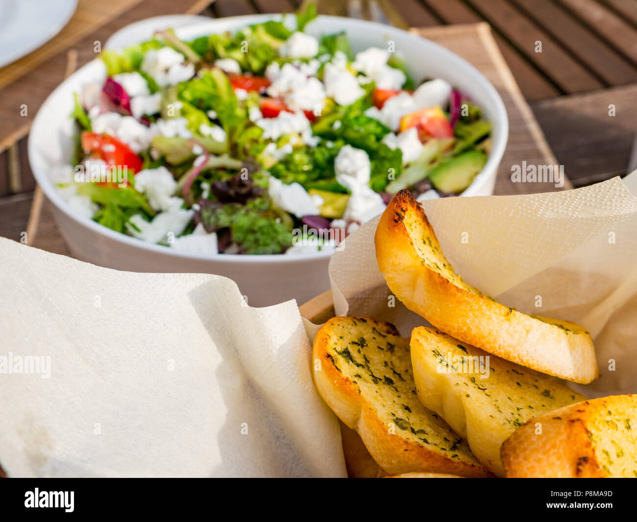 Close up de l'été ensoleillé en salade bol blanc sur la table de patio extérieur, avec laitue, tomates, fromage feta, l'oignon rouge, d'avocat et de pain à l'ail à dorer Banque D'Images