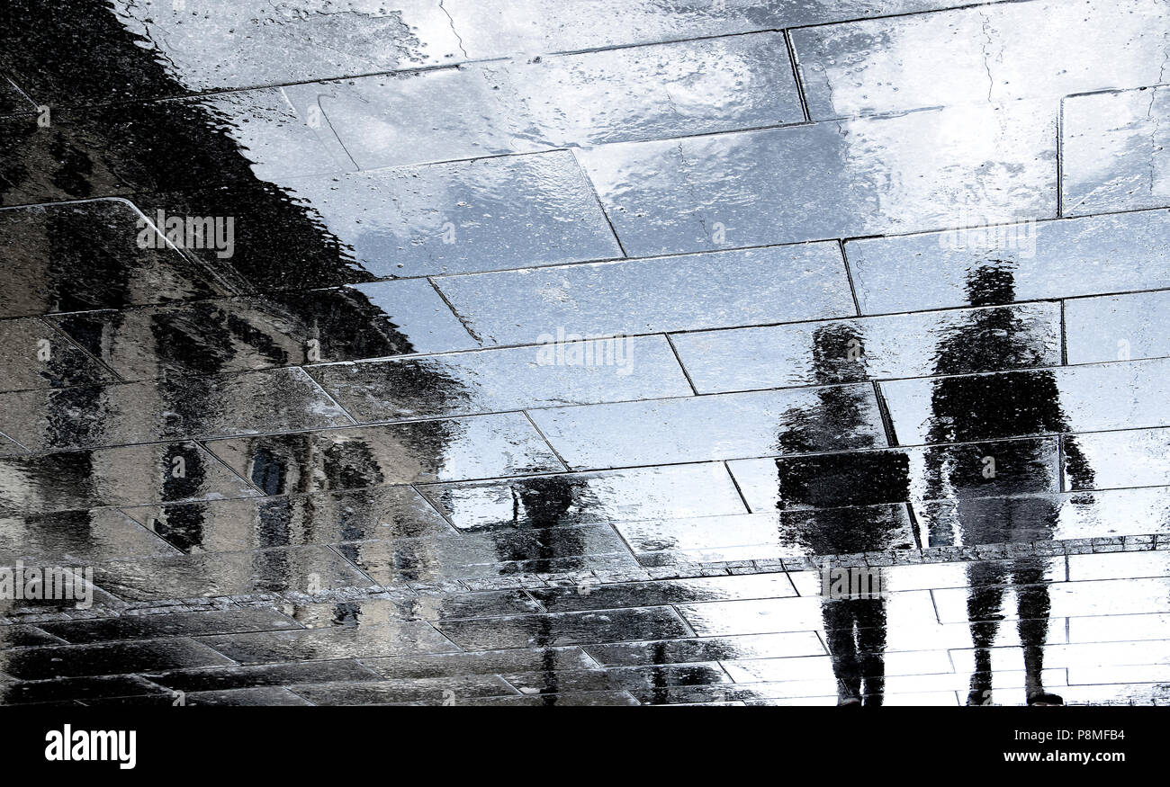 Réflexion floue des silhouettes d'ombre couple walking on the rainy city street Banque D'Images
