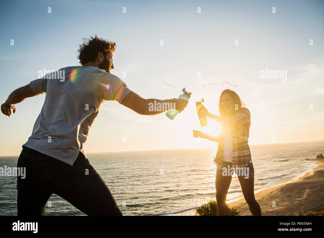 Couple ayant un combat d'eau sur la plage au coucher du soleil Banque D'Images