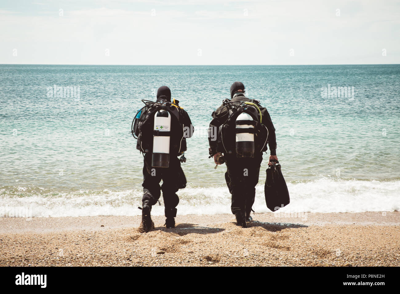 Une vue arrière de deux plongeurs en eau profonde dans l'océan à pied d'une plage sur une plongée en eau profonde Banque D'Images