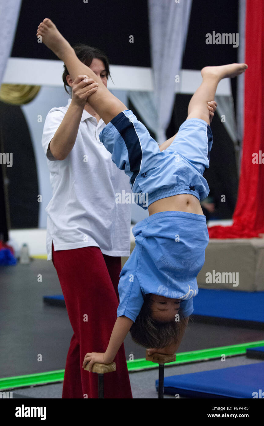 Les pratiques d'un jeune garçon debout sur ses mains en format acrobat school tout en étant repéré par un instructeur. Banque D'Images