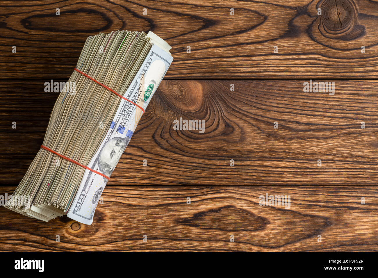 D'épaisseur de wad utilisé 100 dollar bills attachées avec des bandes de caoutchouc debout sur le bord du bois rustique avec copie espace dans une image conceptuelle Banque D'Images
