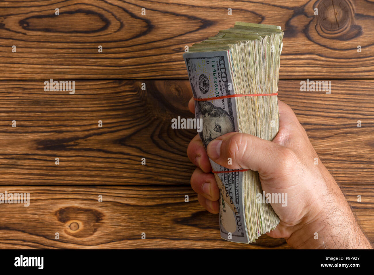 Homme tenant une grande poignée d'empilé 100 dollar bills ou Benjamins agrippa fermement dans son poing sur une table en bois rustique avec copie espace Banque D'Images