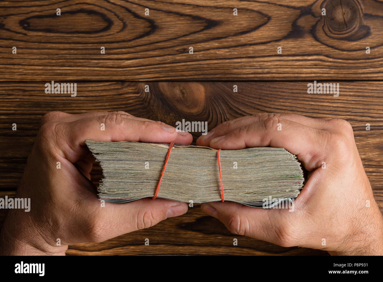 Male hands holding une épaisse liasse d'argent avec bandes de caoutchouc sur une table en bois rustique vue sur le bord du dessus avec copie espace Banque D'Images