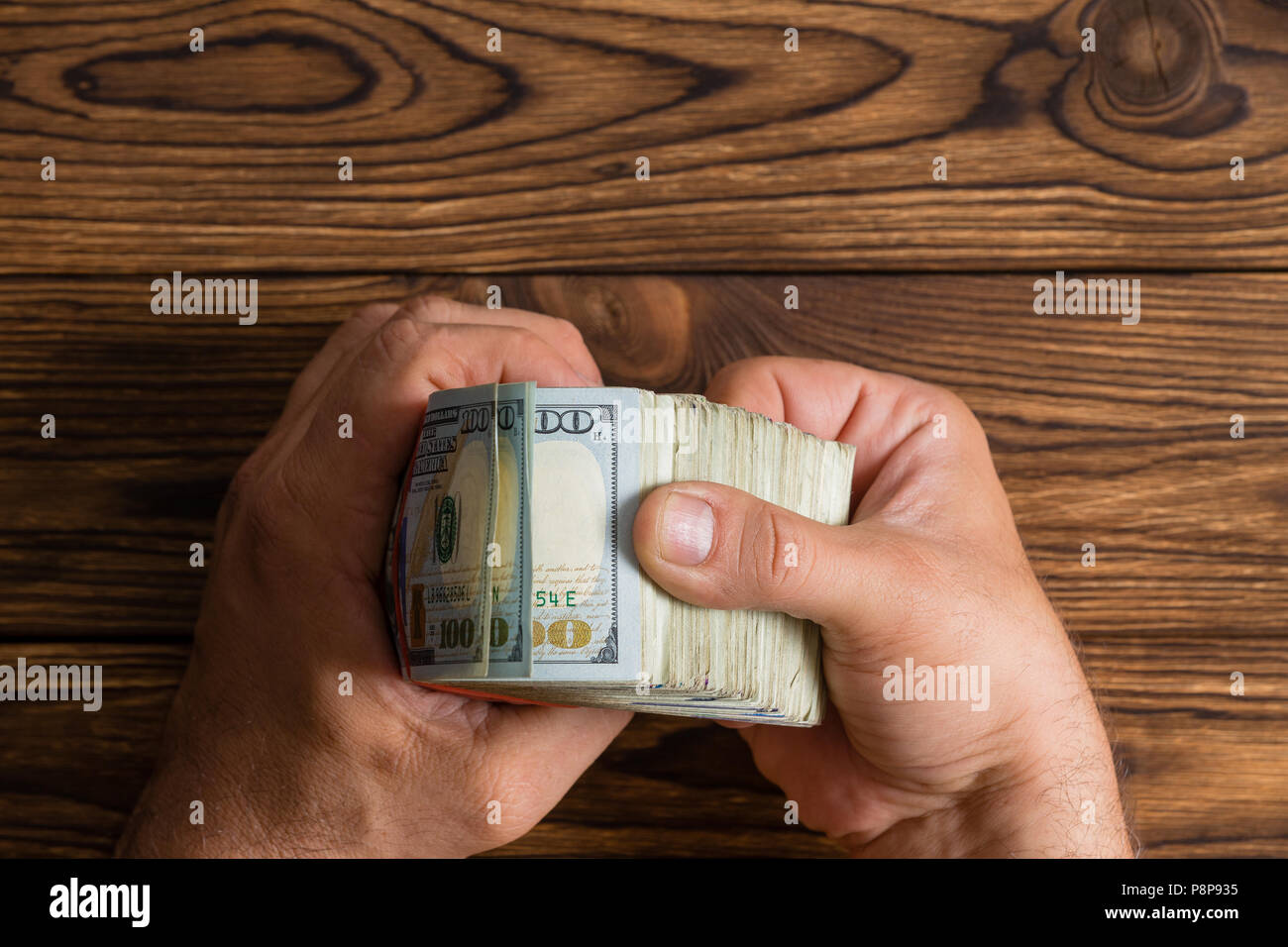 Contrôle de l'homme une épaisse pile de 100 dollar bills feuilleter sur une table en bois rustique avec copie espace Banque D'Images