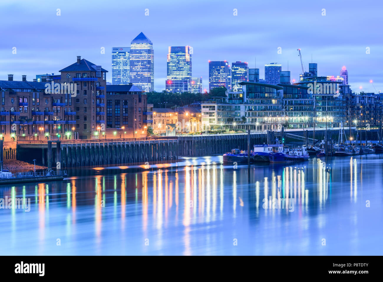 Vue avant l'aube du Tower Bridge vers l'allumé en immeubles de Canary Wharf, London, avec des lumières reflétées dans la Tamise Banque D'Images