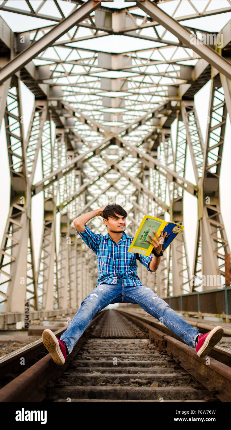 Jeune adulte Jeune Indien étonné en lisant un livre pendant que léviter sur des rails de chemin de fer sous le pont ferroviaire métallique. Banque D'Images