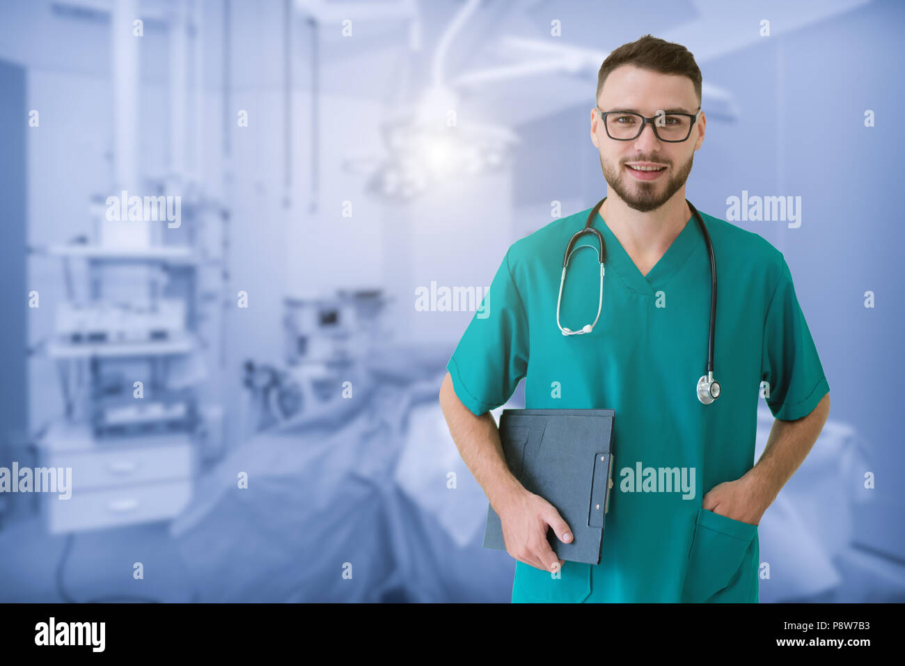 Beau jeune médecin est looking at camera, dans une salle d'opération moderne à l'hôpital. Banque D'Images