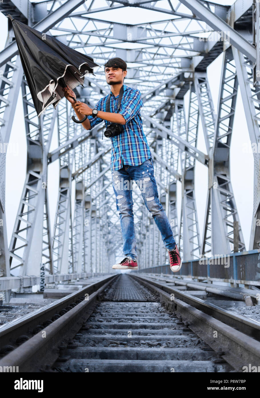 Jeune adulte Jeune Indien léviter sur voie ferrée avec parapluie en main et appareil photo sur le cou sous la structure du pont métallique. Banque D'Images