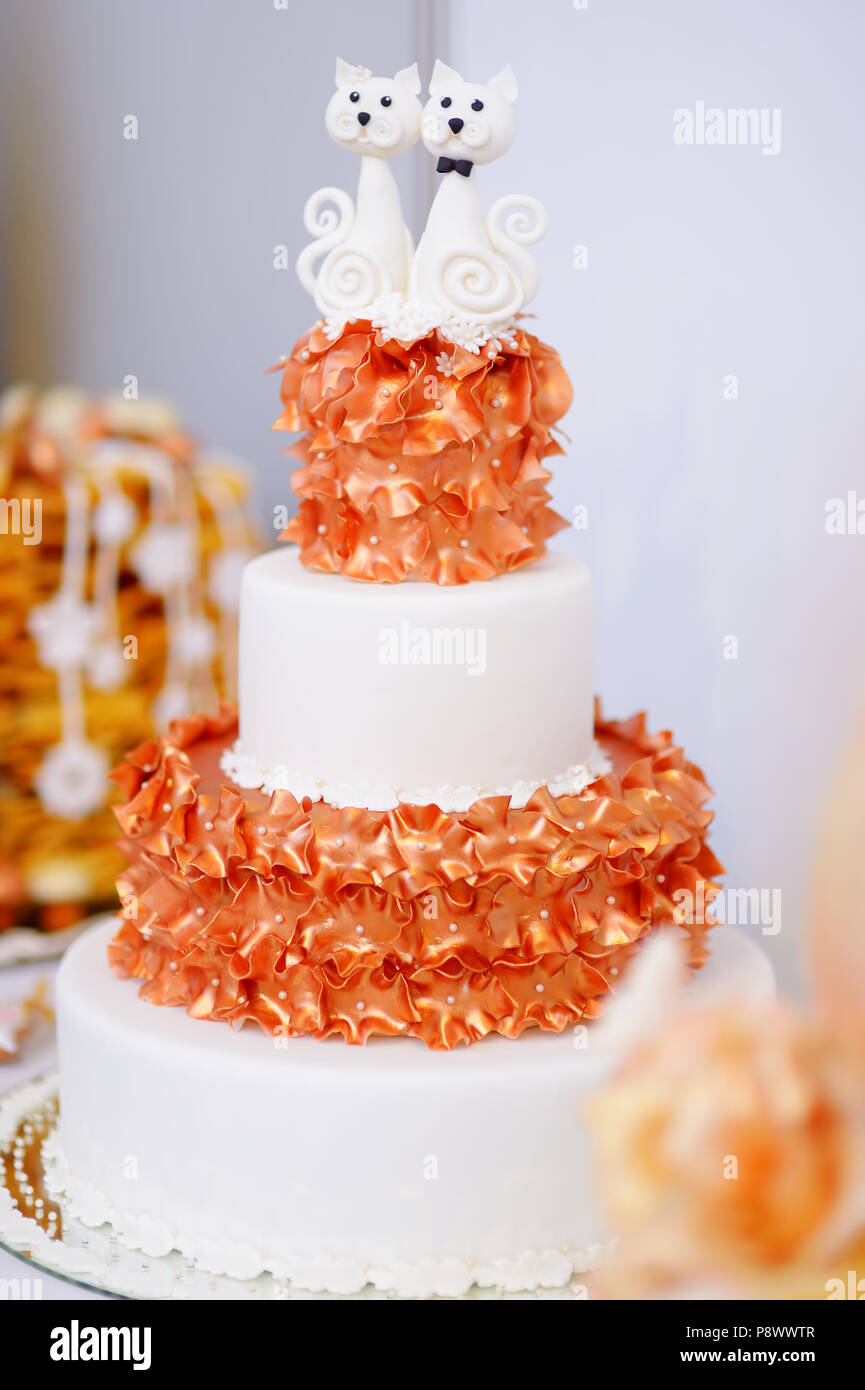 Gâteau de mariage blanc décoré de fleurs de sucre orange et deux matous de sucre sur le dessus Banque D'Images