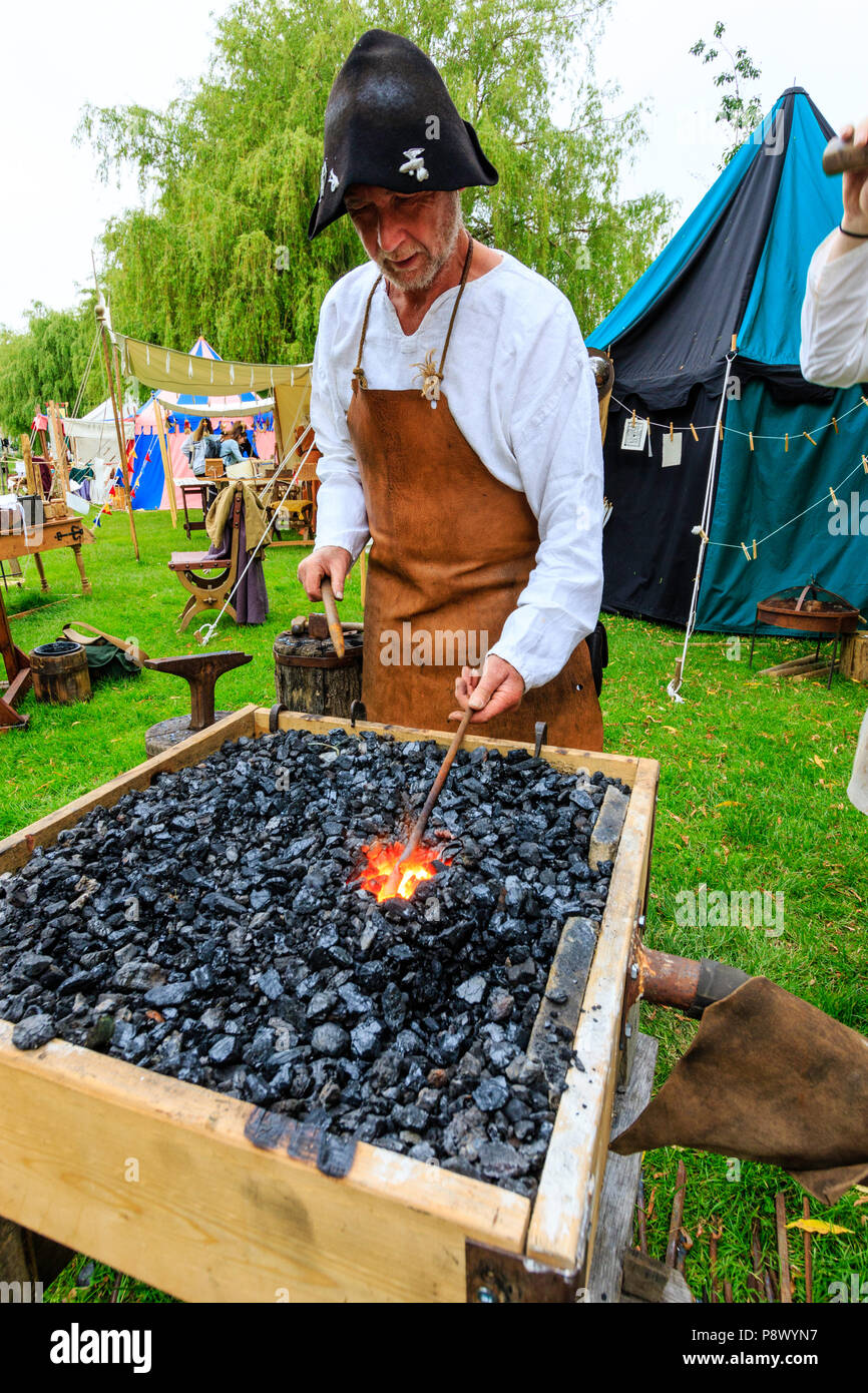 L'histoire vivante, une reconstitution d'un événement. L'homme médiéval, forgeron, à l'aide de forge pour faire des armes de fer, holding longueur de métal. Banque D'Images