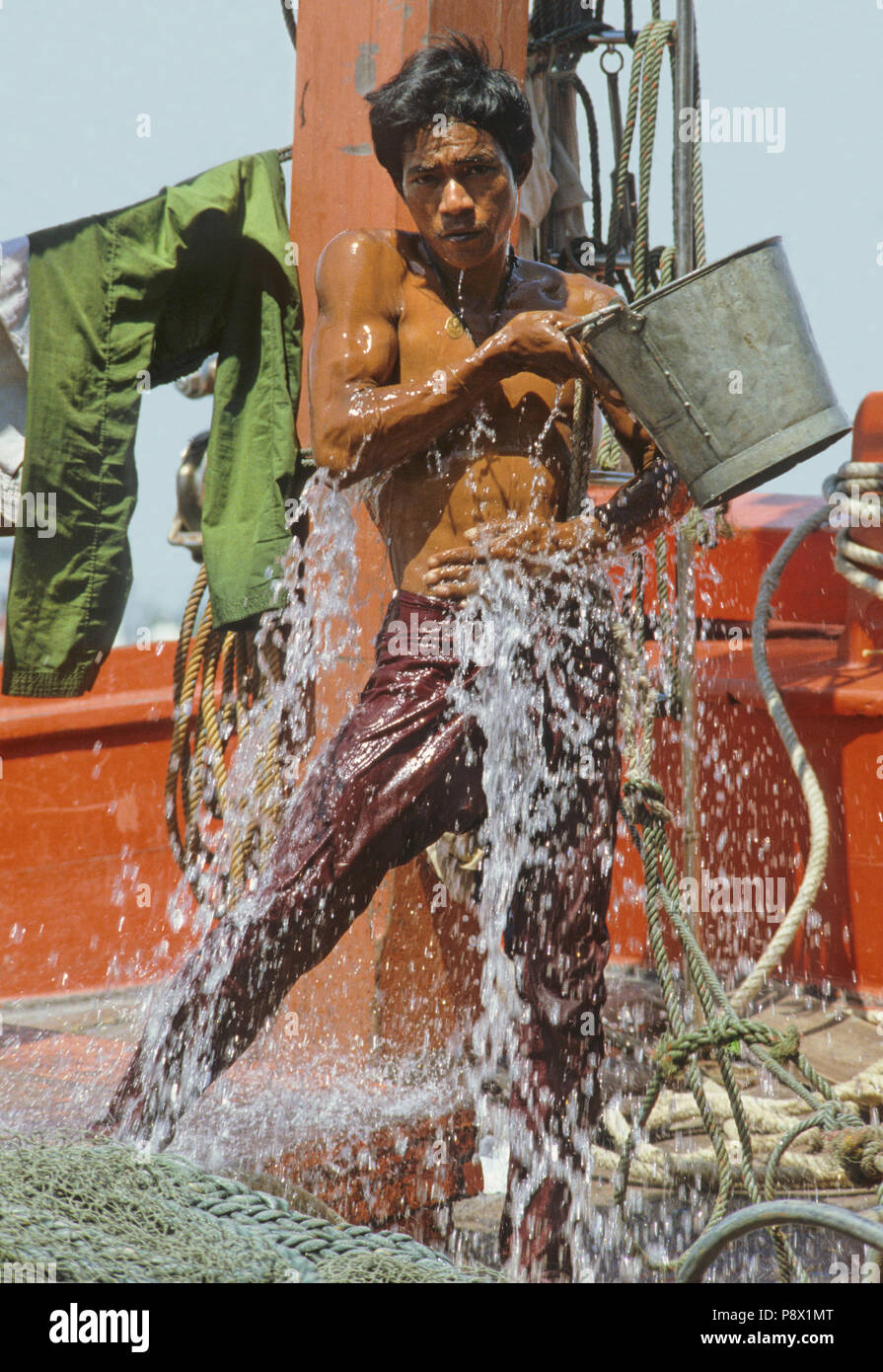 Un jeune matelot swills lui-même avec un seau d'eau sur le pont de son bateau de pêche à Bangkok Banque D'Images
