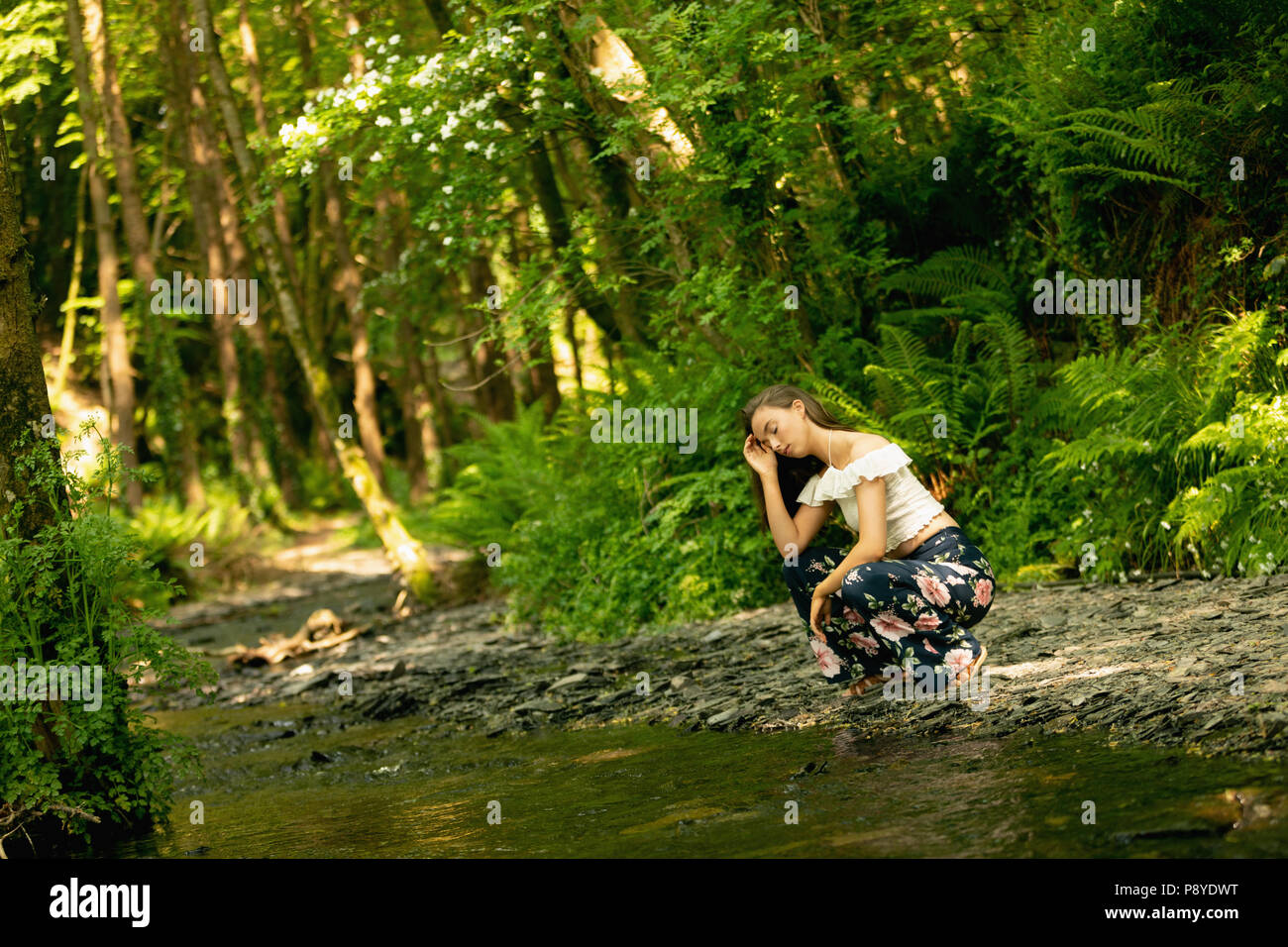 Femme accroupie près de la côte de la rivière dans la forêt verte Banque D'Images