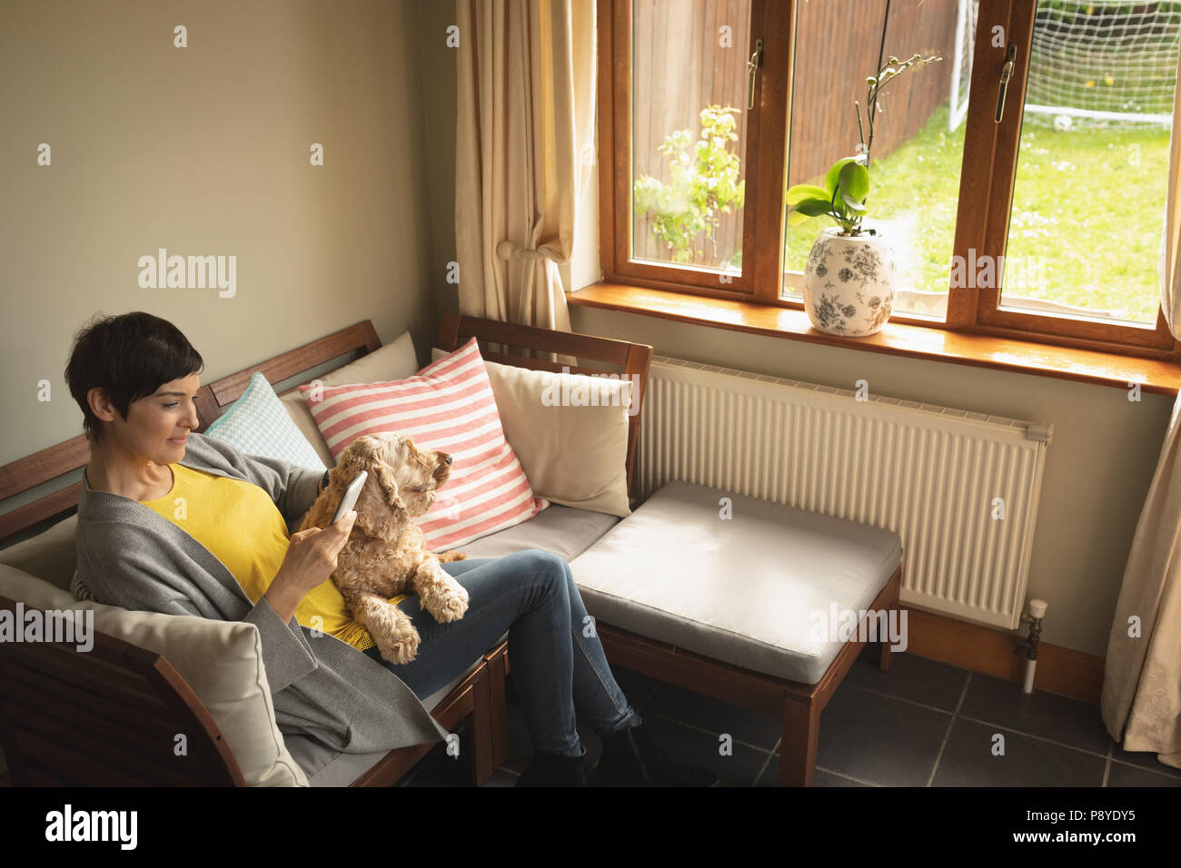 Woman using mobile phone with dog on sofa in living room Banque D'Images
